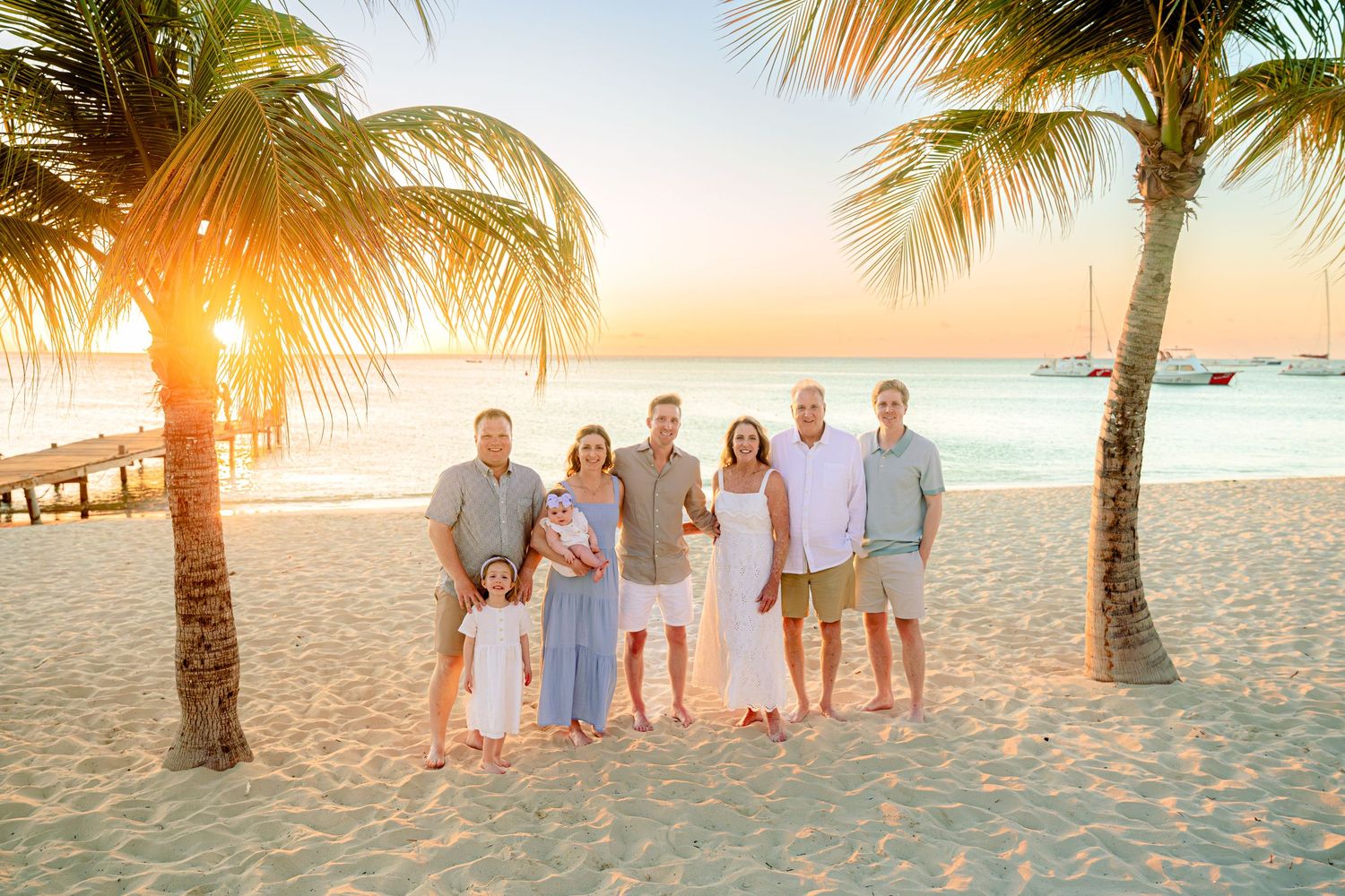 Family group photo at sunset on a tropical beach with palm trees, golden light, and calm turquoise waters in the background.