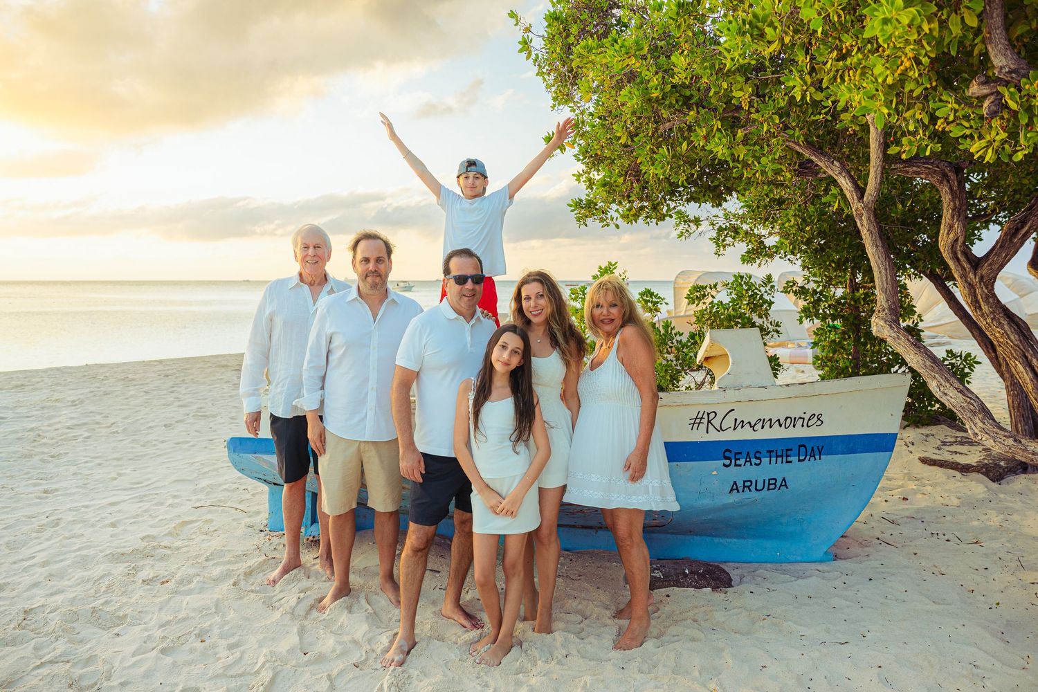 Family posing together near a colorful boat on a sandy Aruba beach at sunset.