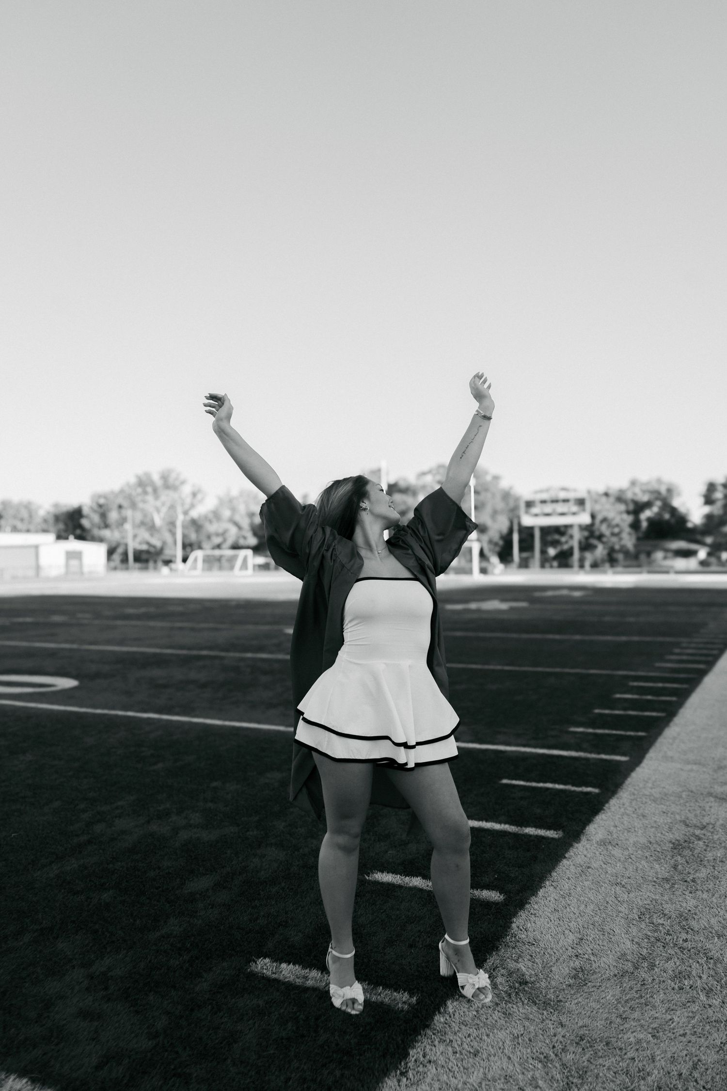 Black and white photo of graduate celebrating with arms raised on football field.