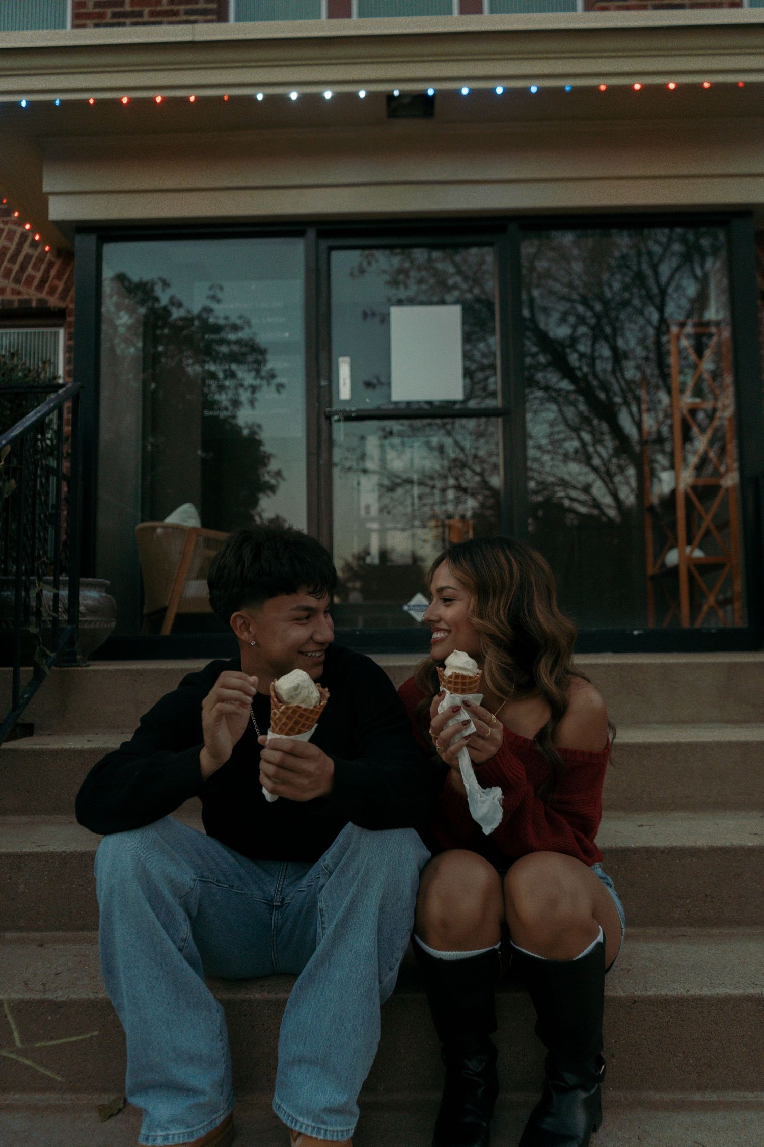 Smiling couple sharing ice cream cones while sitting on steps outside a building at dusk.