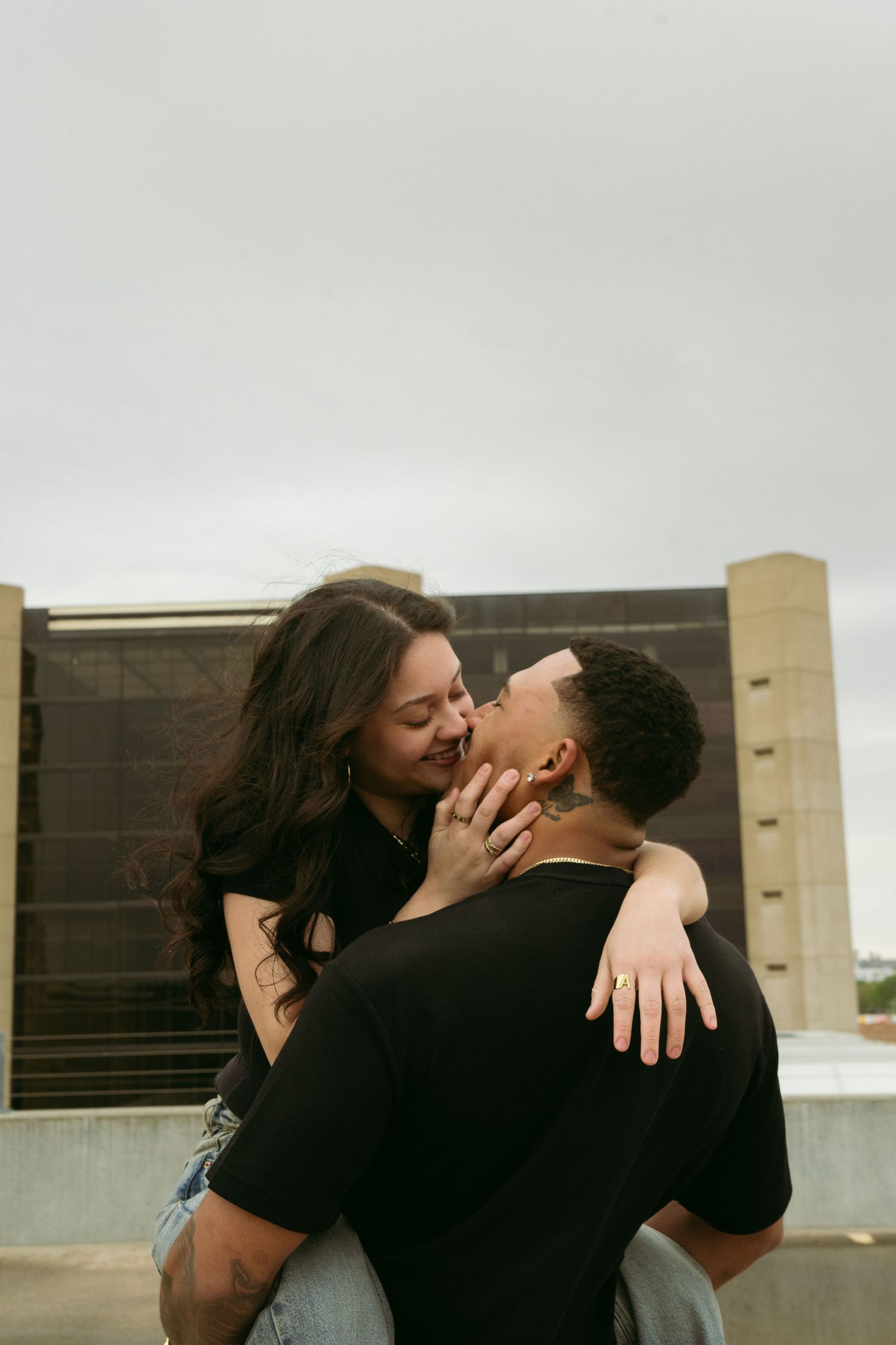 Romantic couple about to kiss on a rooftop, woman sitting on mans lap with arms around him.