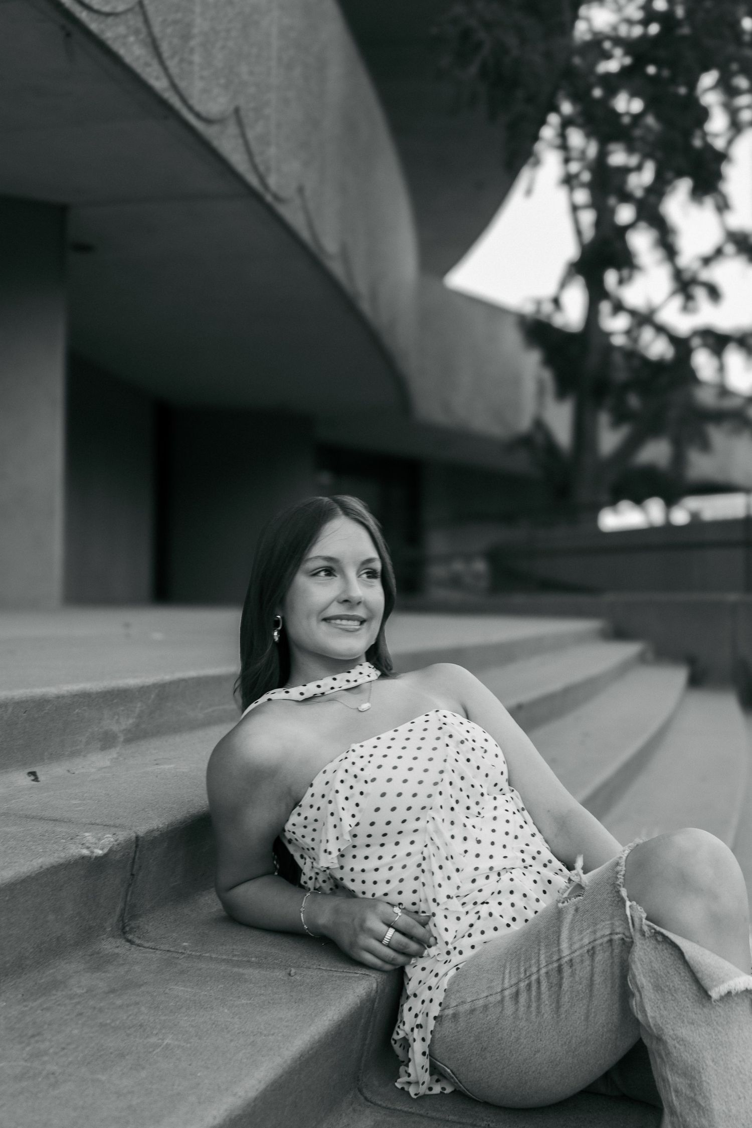 Black and white photo of young woman in polka dot top relaxing on concrete steps outdoors.