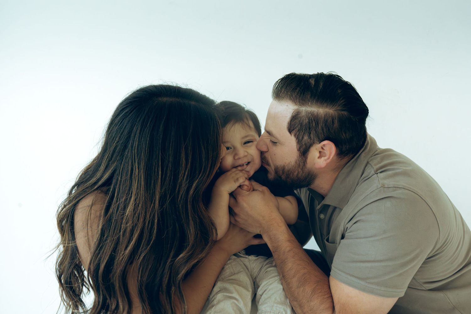 Loving parents kissing and cuddling their smiling toddler son in a studio.