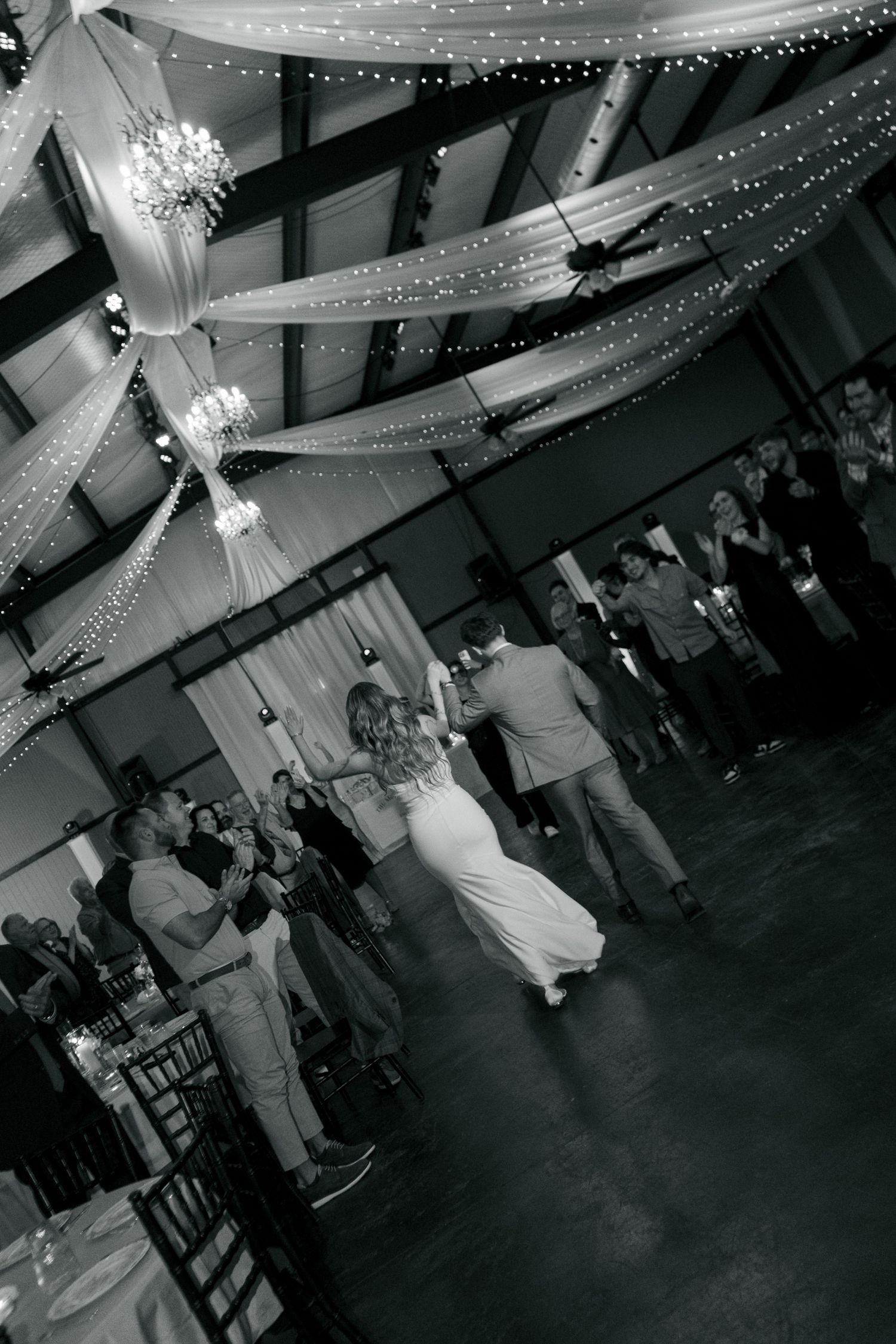Black and white photo of a bride and groom sharing their first dance at a decorated wedding reception venue.