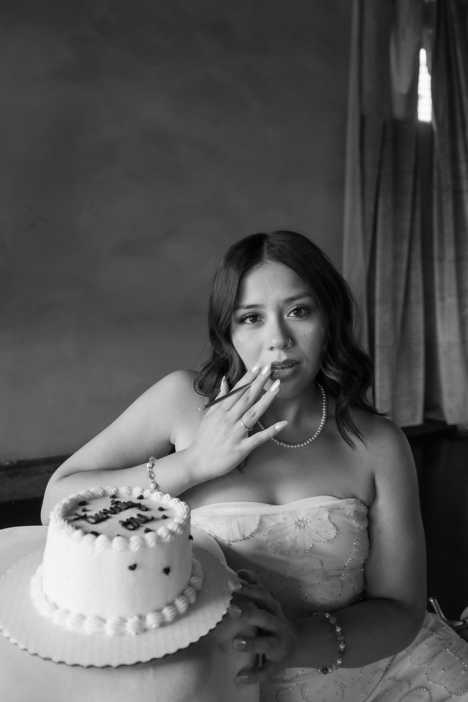 Black and white photo of a bride in strapless gown tasting wedding cake, wearing pearl necklace and bracelet.