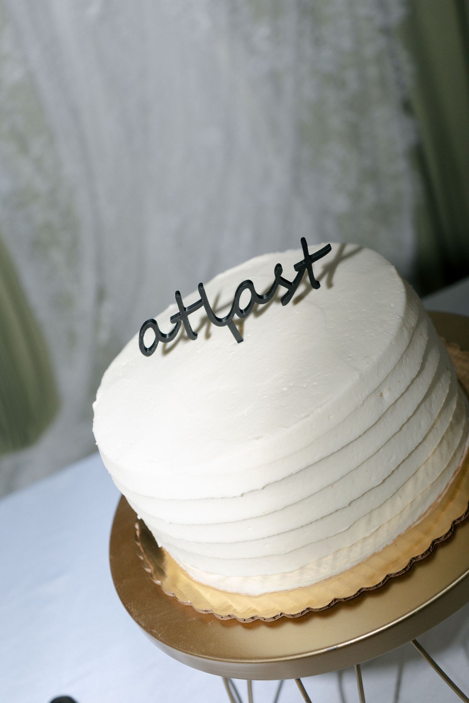 Elegant white textured wedding cake with black script at last topper on a gold stand.