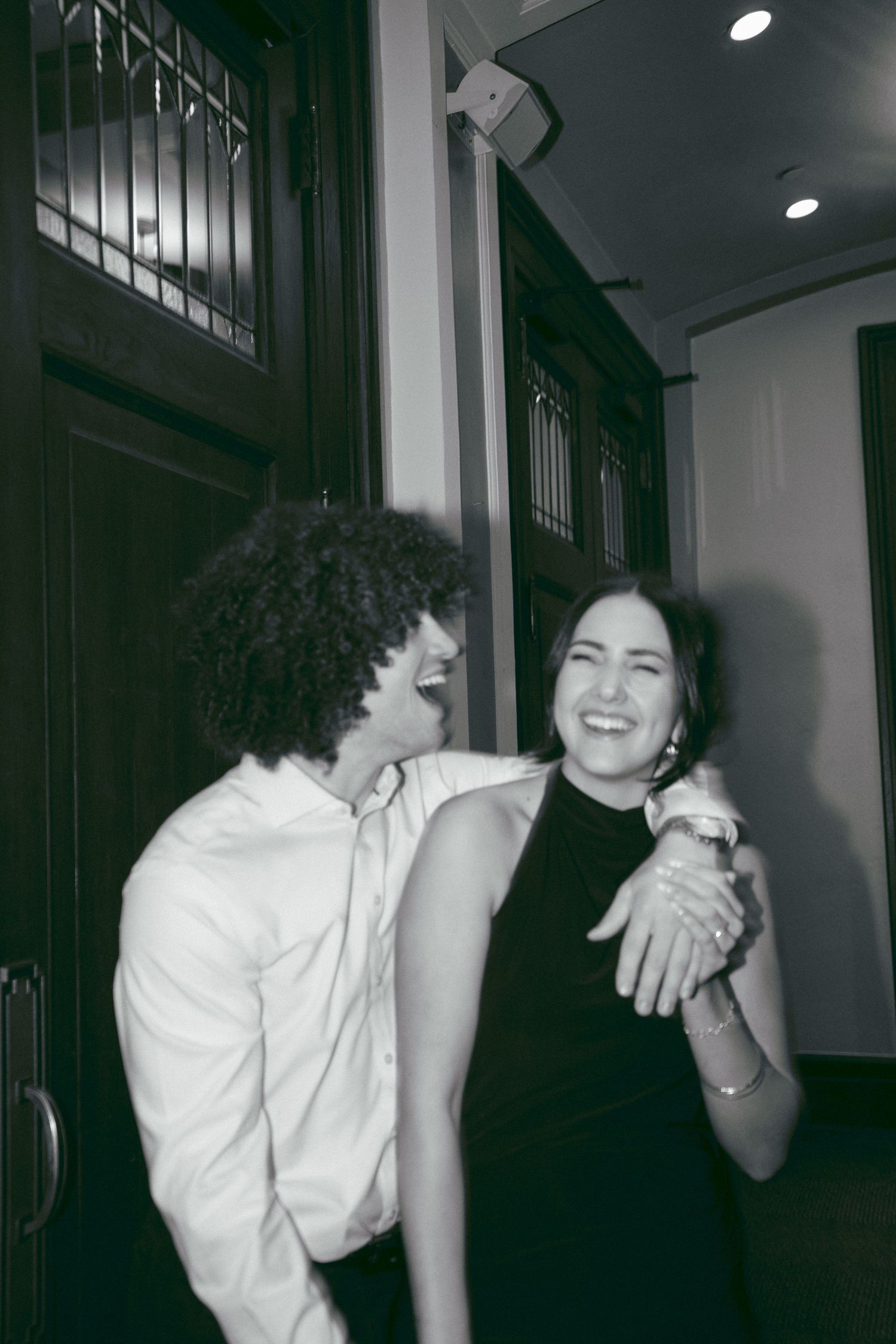 Couple laughing together in hallway, woman showing engagement ring, black and white photo.