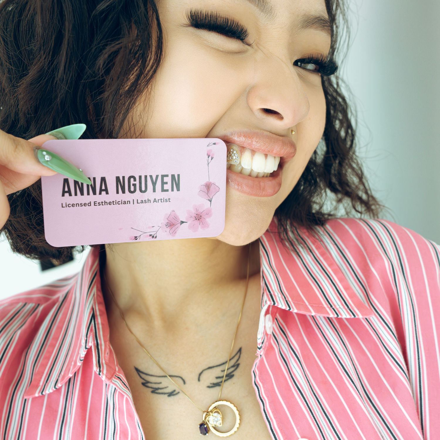 Woman smiling and holding a pink business card for Anna Nguyen, Licensed Esthetician and Lash Artist.