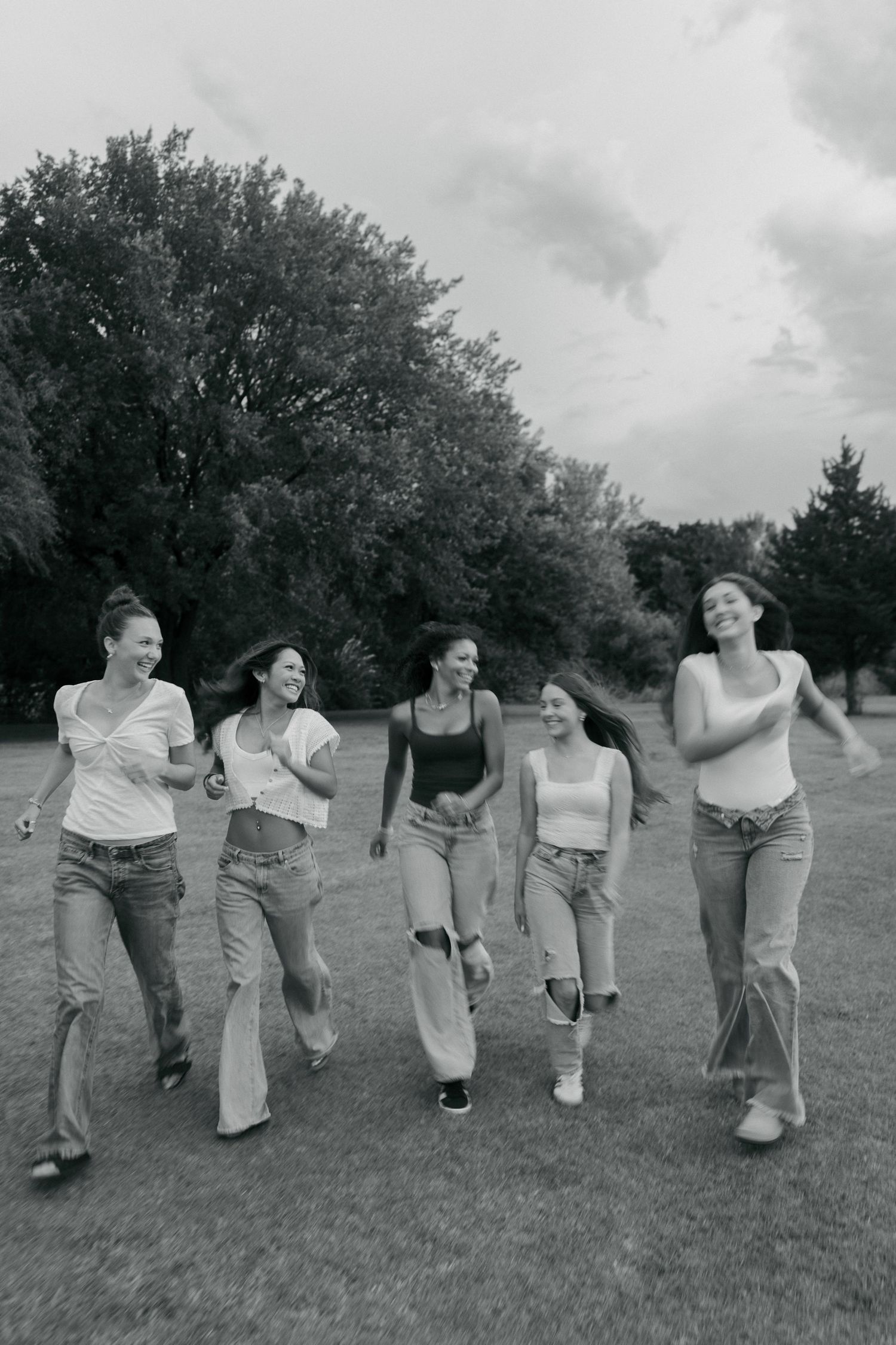 Five young women laughing and walking together through a park in black and white photo.
