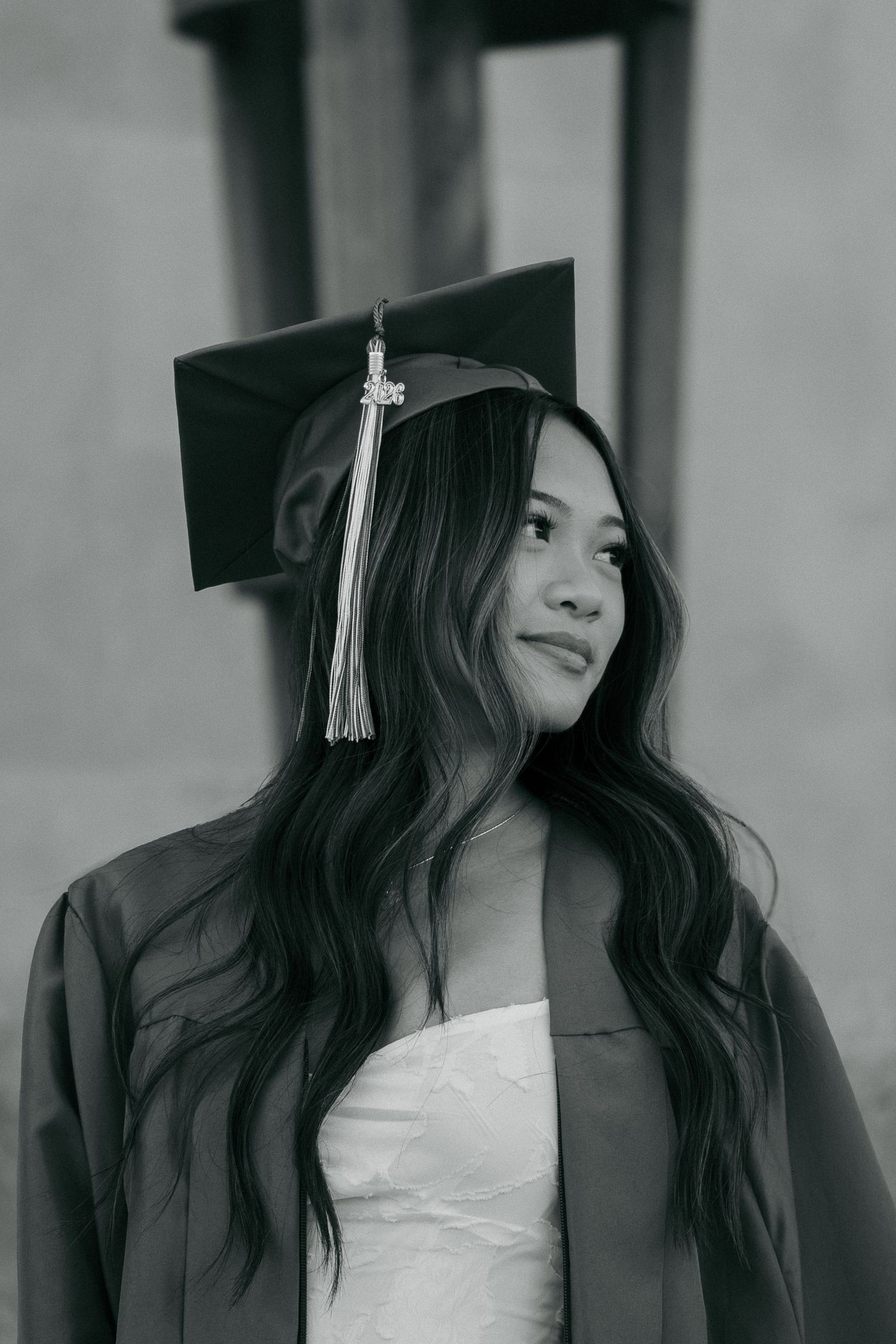 Black and white portrait of young woman in graduation cap and gown looking away.