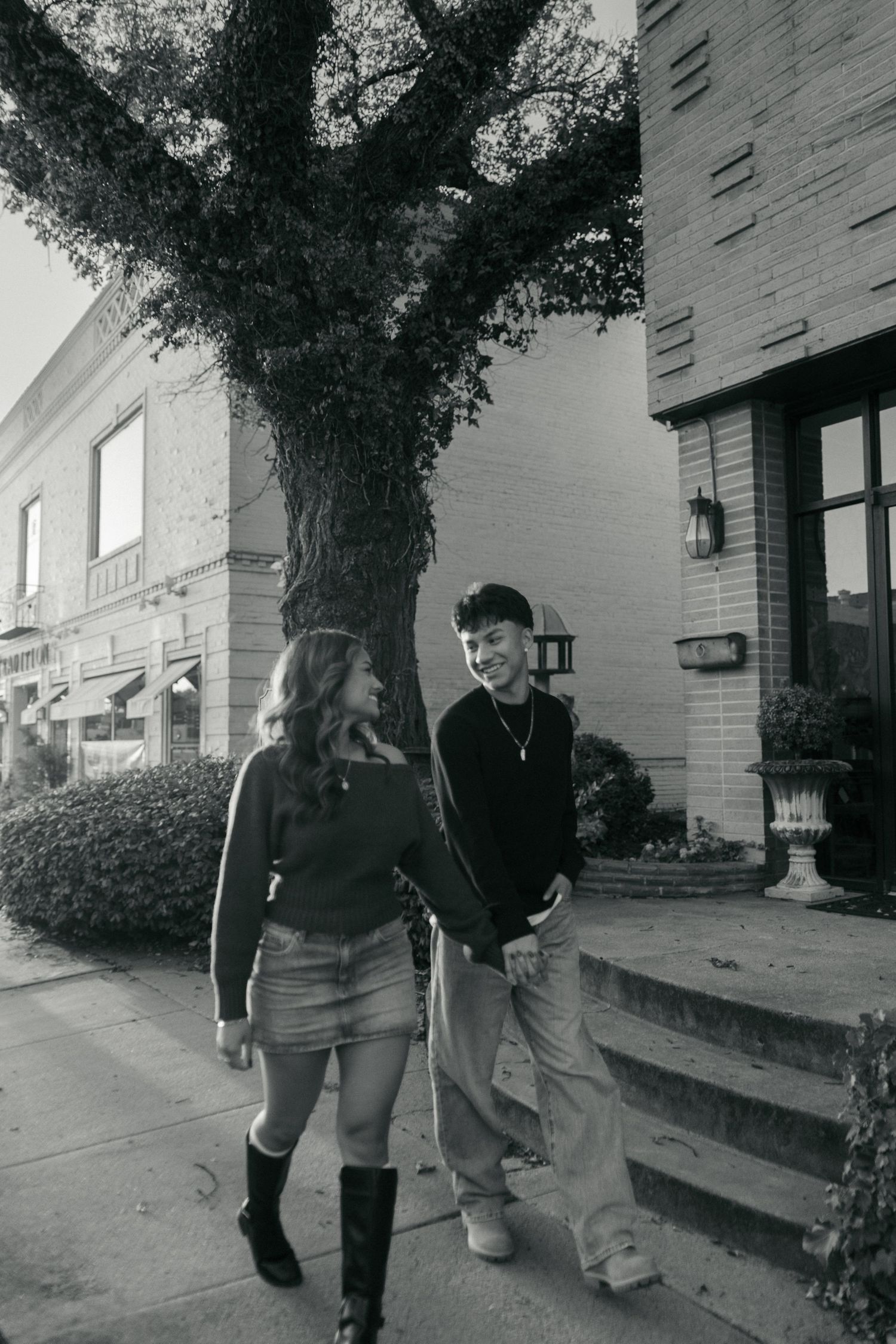 Young couple smiling and walking together on a sidewalk in black and white urban street photo.