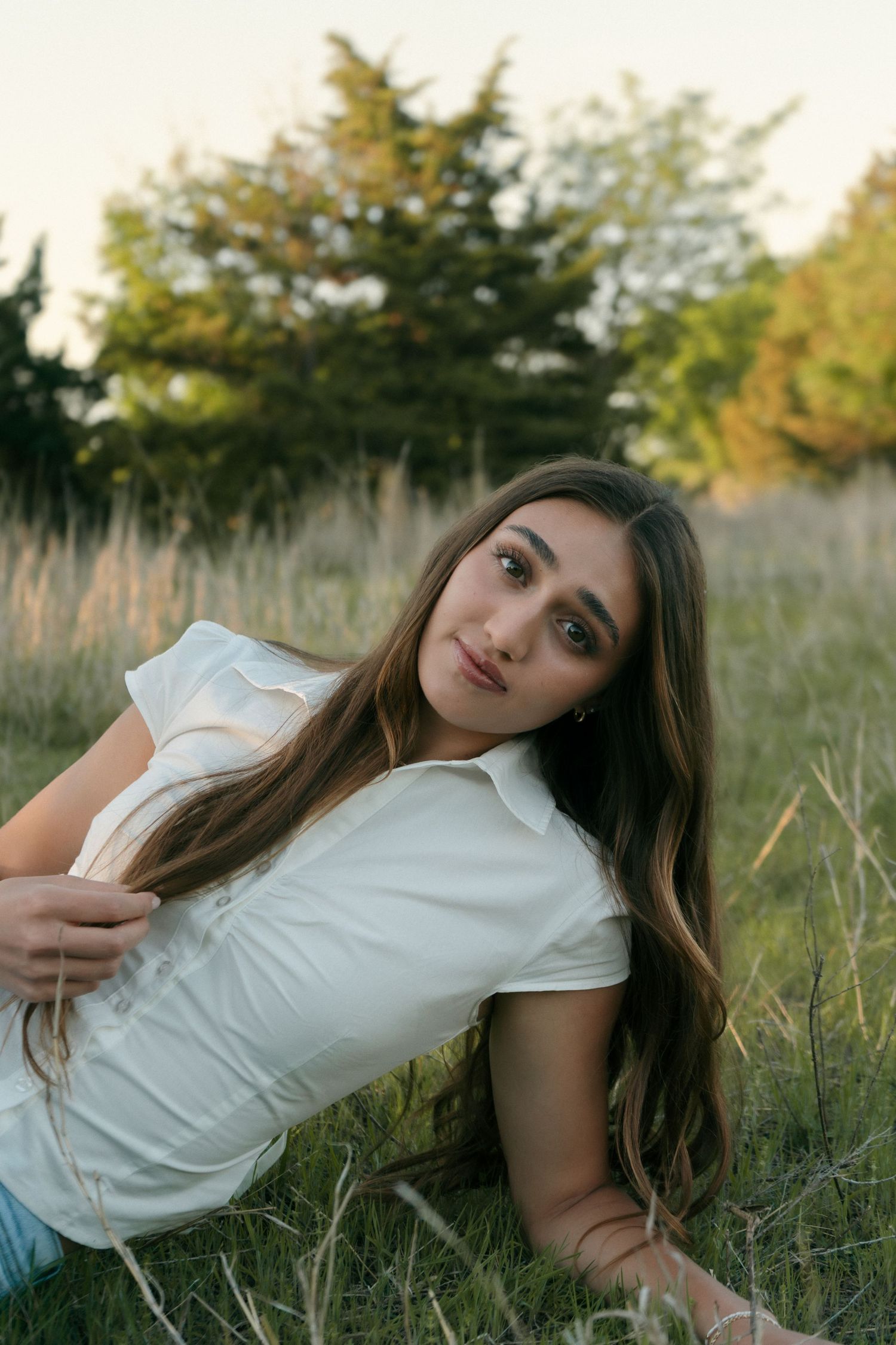 Young woman with long brown hair lying in green grass field during golden hour sunset.
