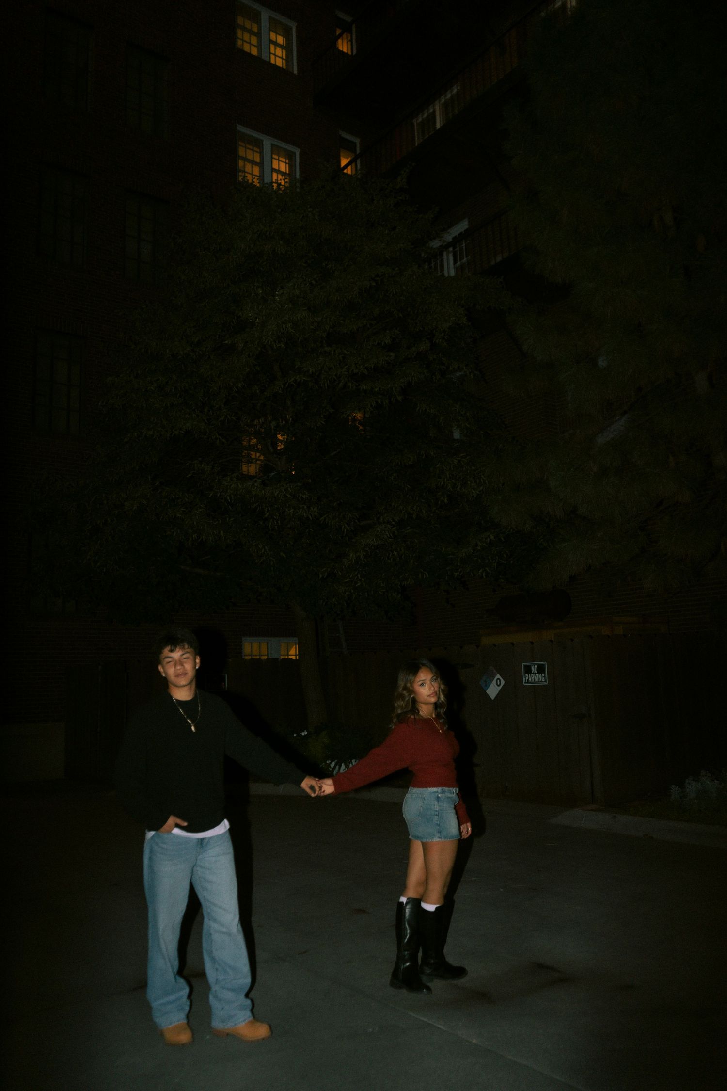 A young couple holds hands while posing together on a dark outdoor pathway at night.