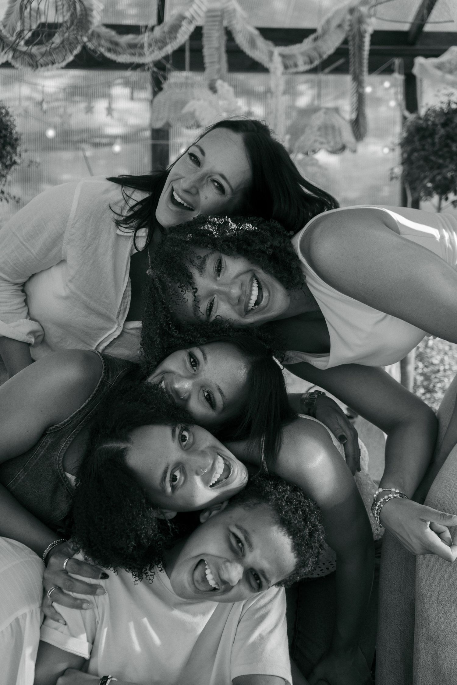 Black and white photo of five diverse women smiling and leaning heads together in a joyful group pose.