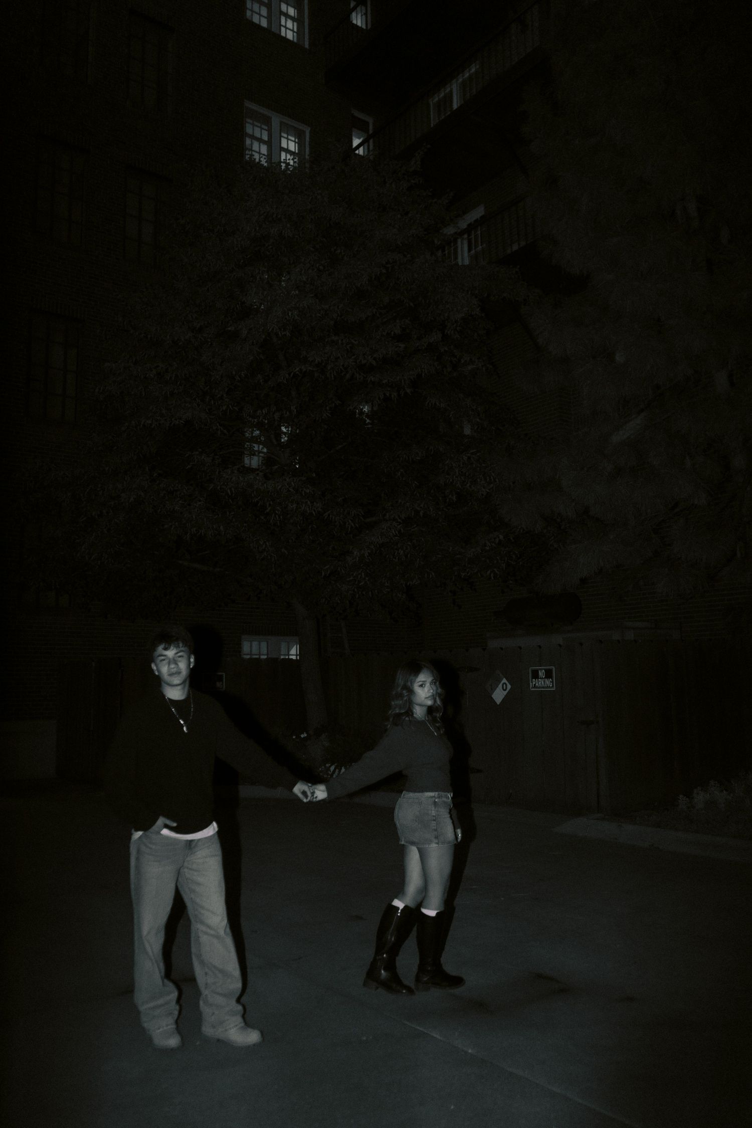 A black and white photo of a couple holding hands outdoors at night near a tall building.