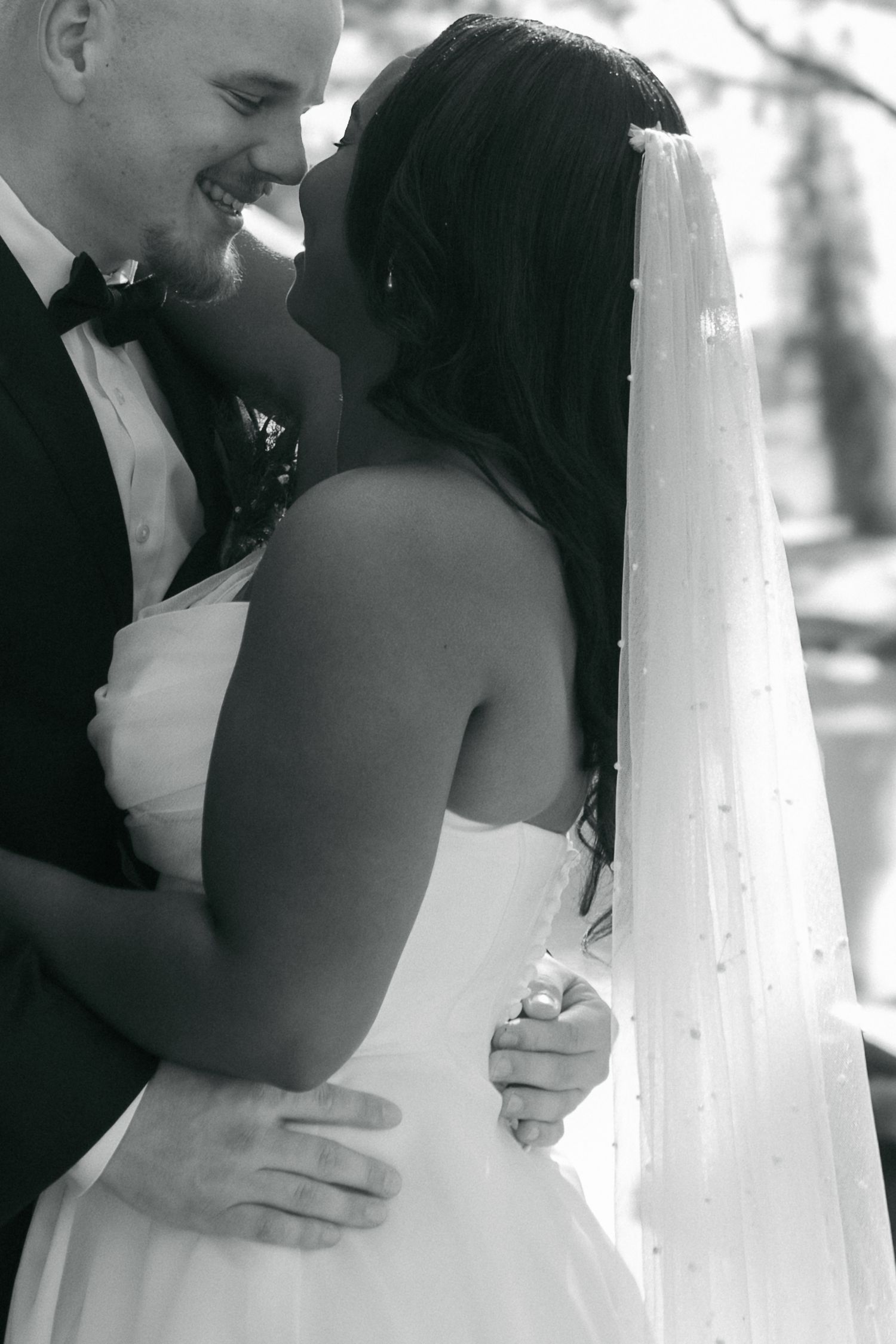 Black and white close-up of bride in veil and groom smiling intimately during wedding portraits.