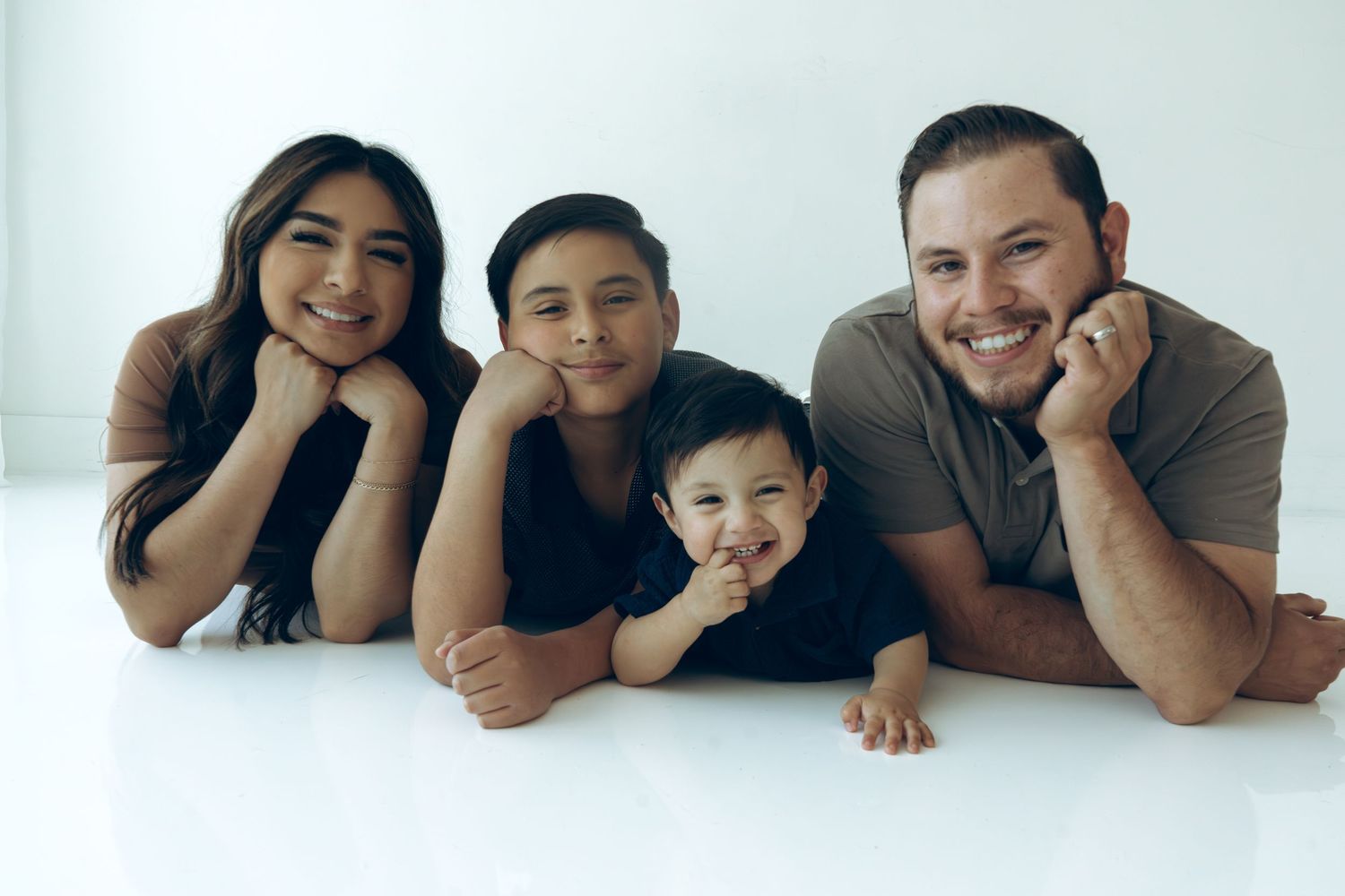 Cheerful family of four lying on floor smiling at camera in white studio.
