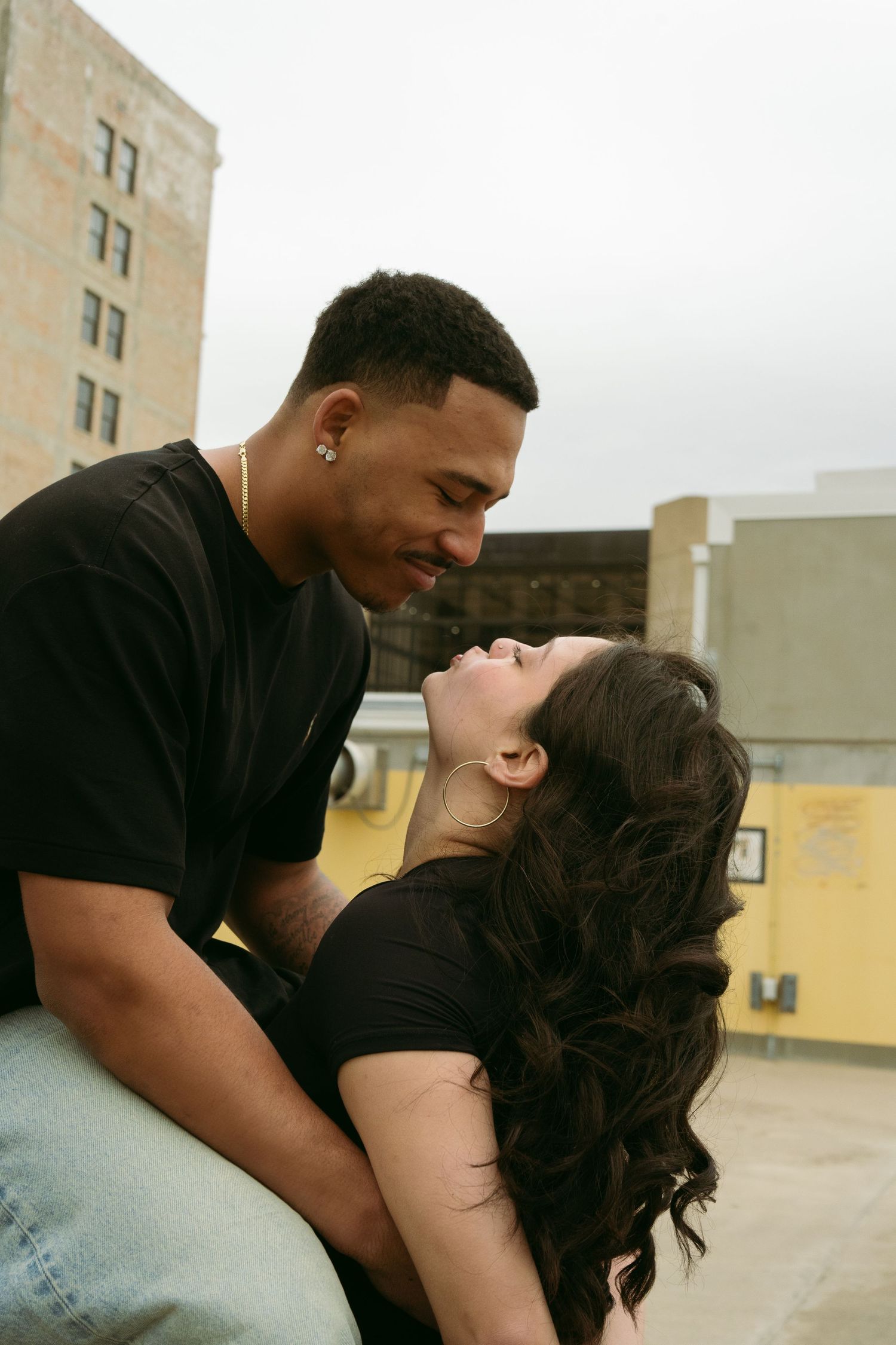 Romantic interracial couple sharing a tender moment on a rooftop in casual black outfits.