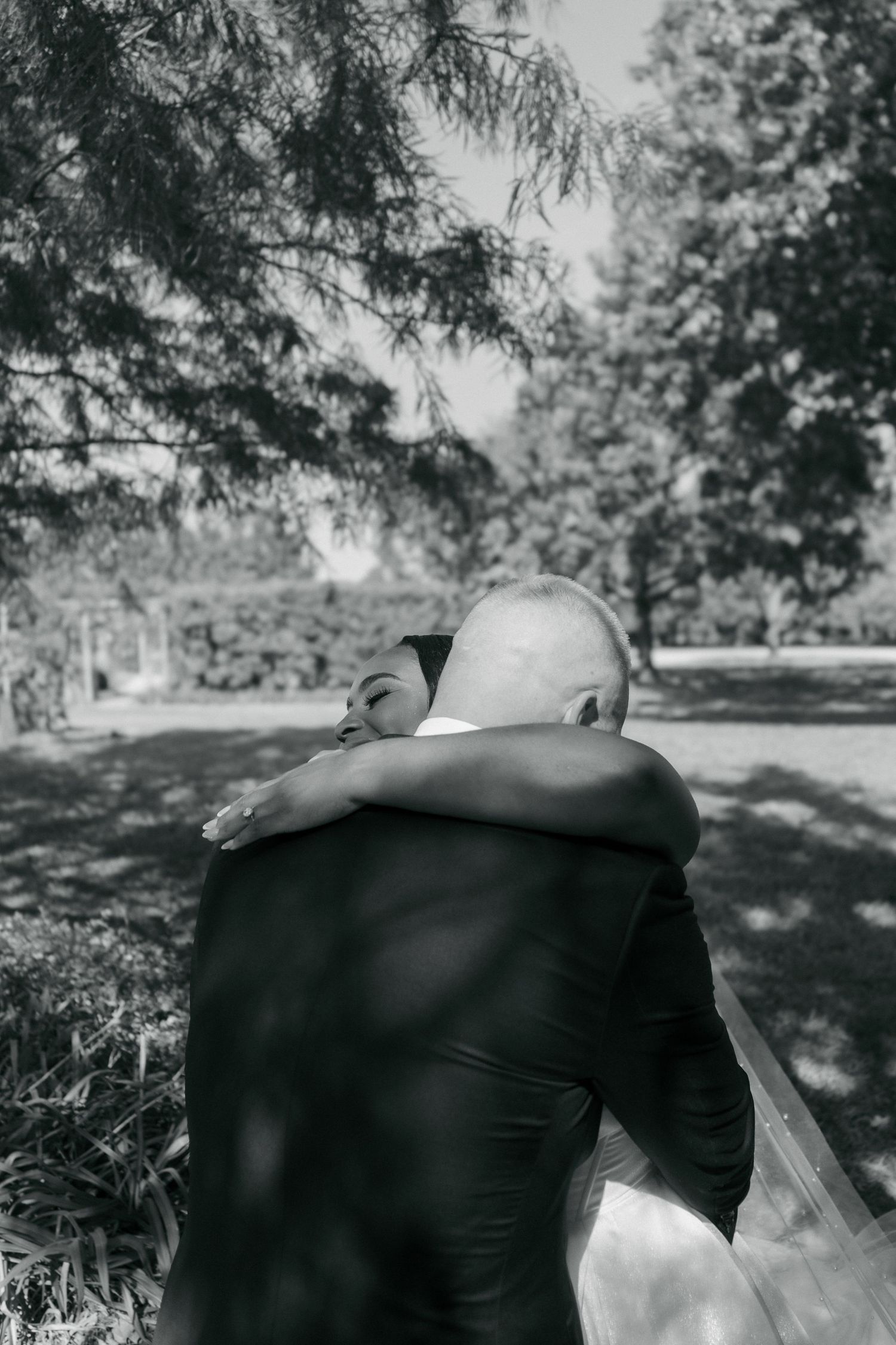 Black and white photo of bride and groom sharing an emotional embrace outdoors on their wedding day.