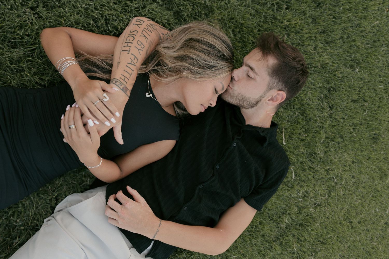 Couple lying on green grass, sharing a tender nose kiss while embracing.