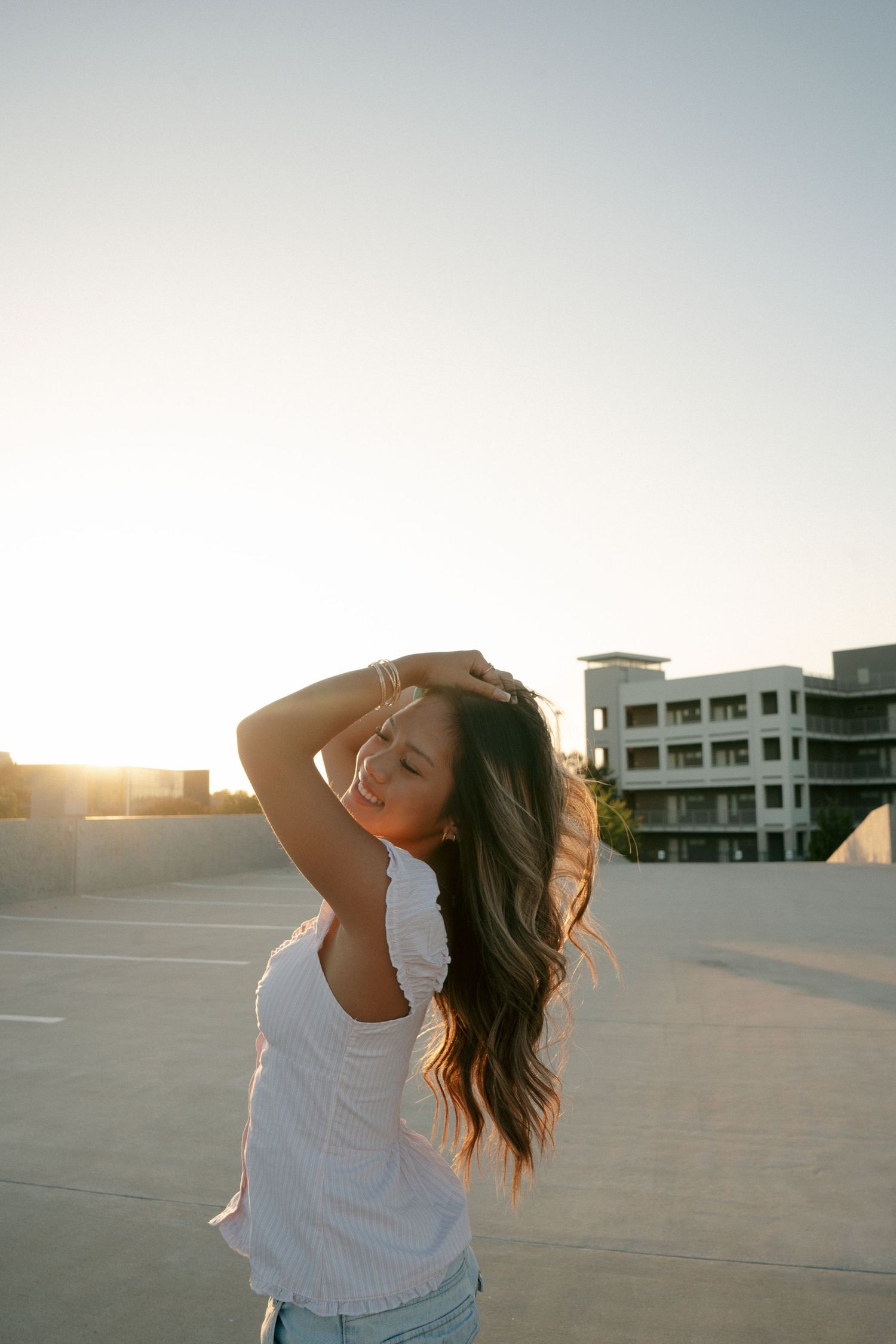 Young woman with long hair posing on rooftop at sunset with golden backlight glowing behind her.