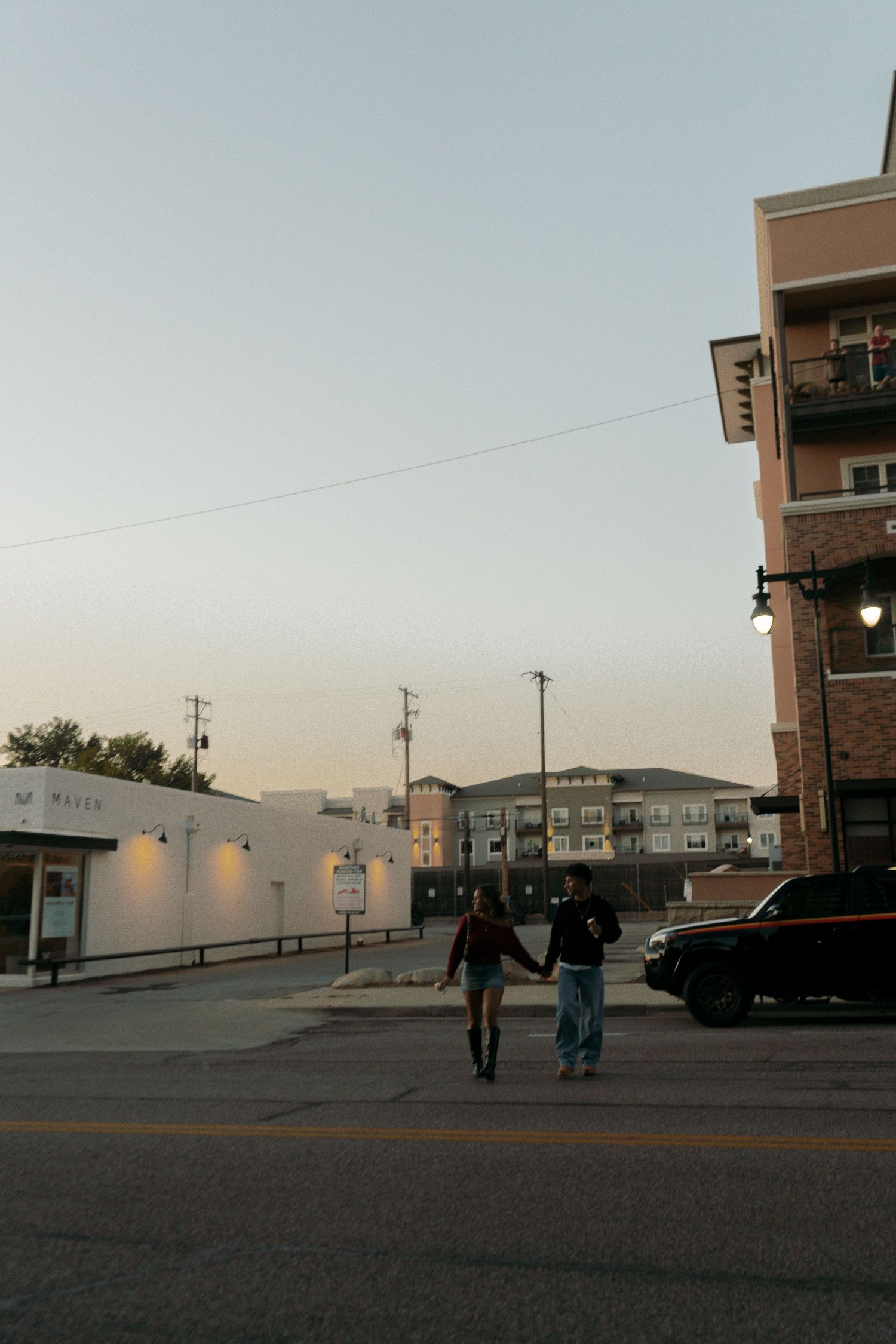Couple holding hands while crossing a street at sunset in an urban neighborhood setting.