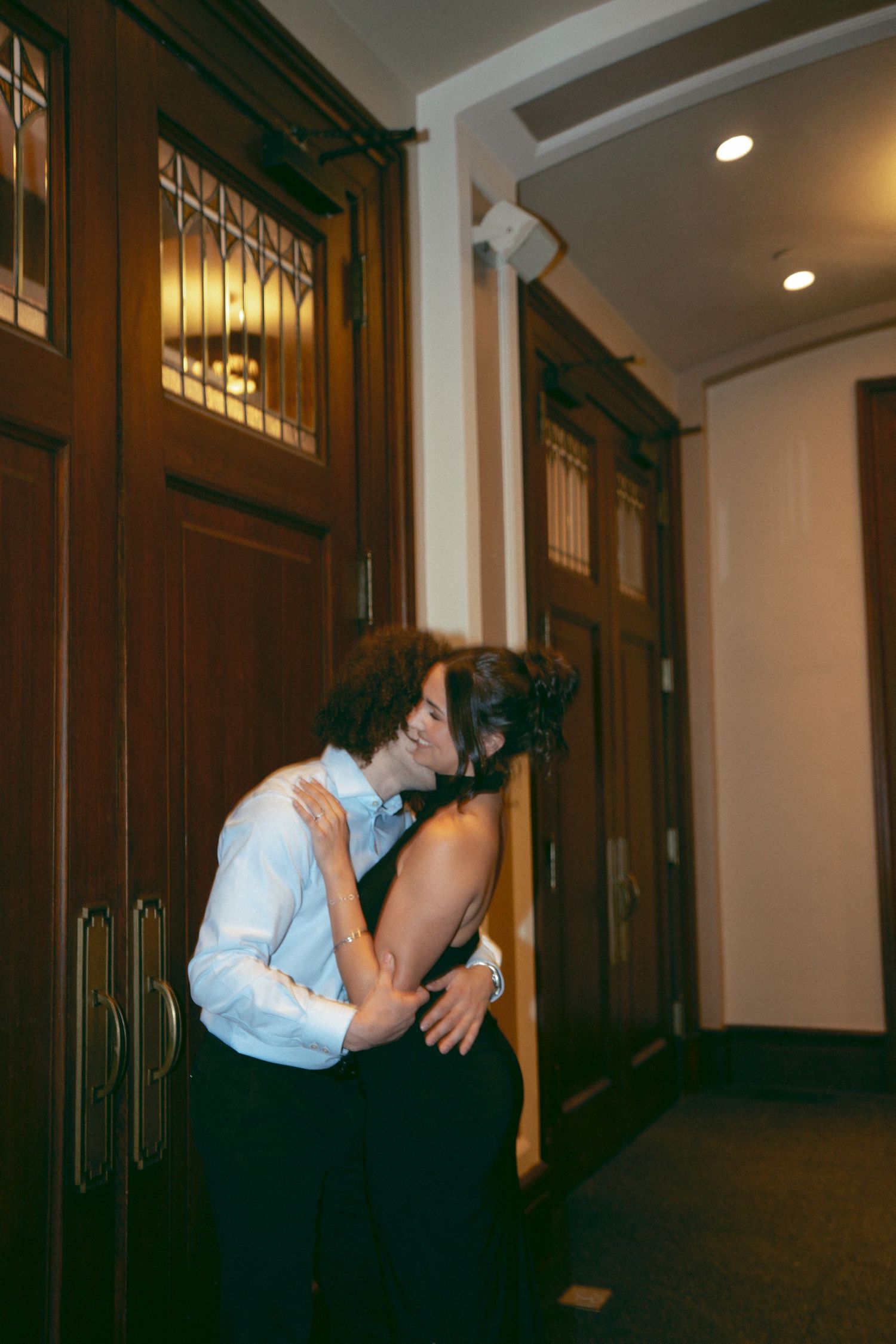 Couple sharing a romantic kiss in a warmly lit hallway with wooden doors.