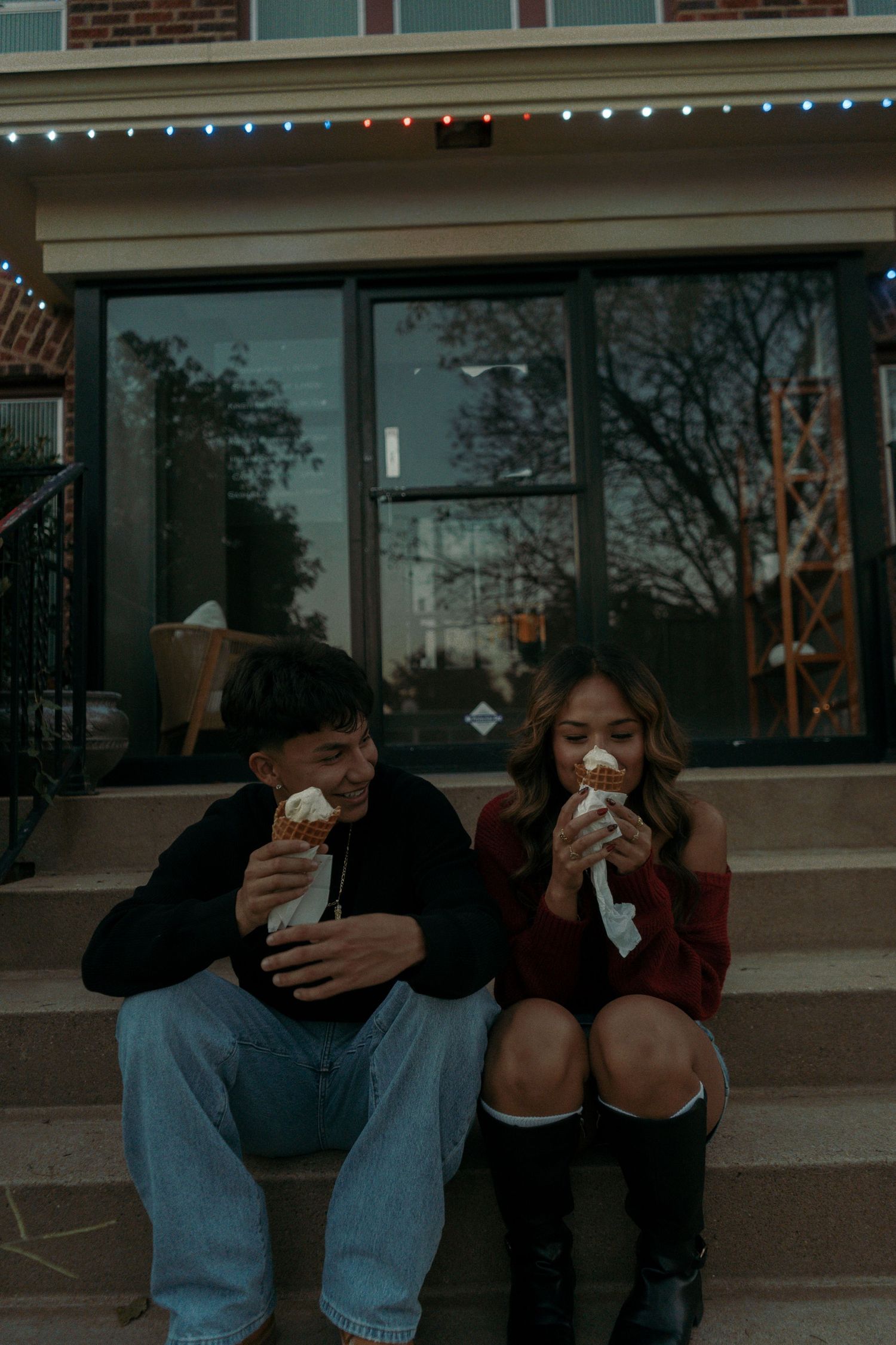 Young couple sitting on outdoor steps enjoying ice cream cones together in the evening light.