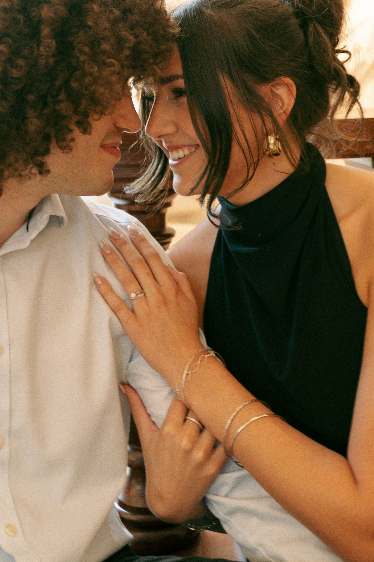 Happy couple gazing at each other, woman displaying diamond engagement ring in warm light.