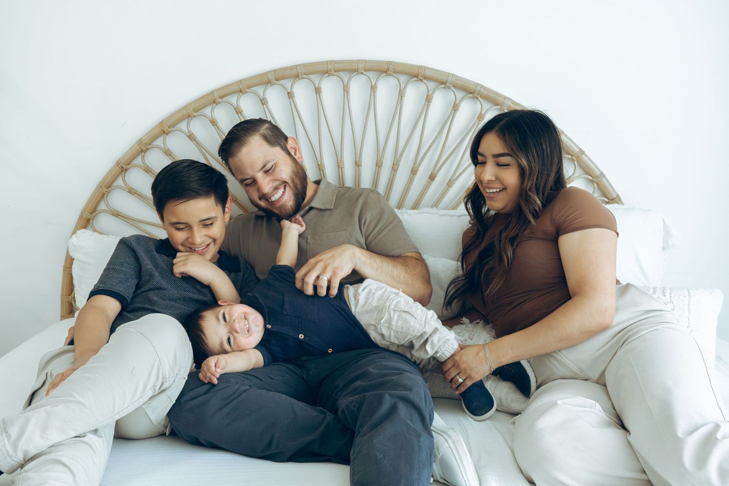 Happy family of four relaxing together on a white couch with rattan headboard.