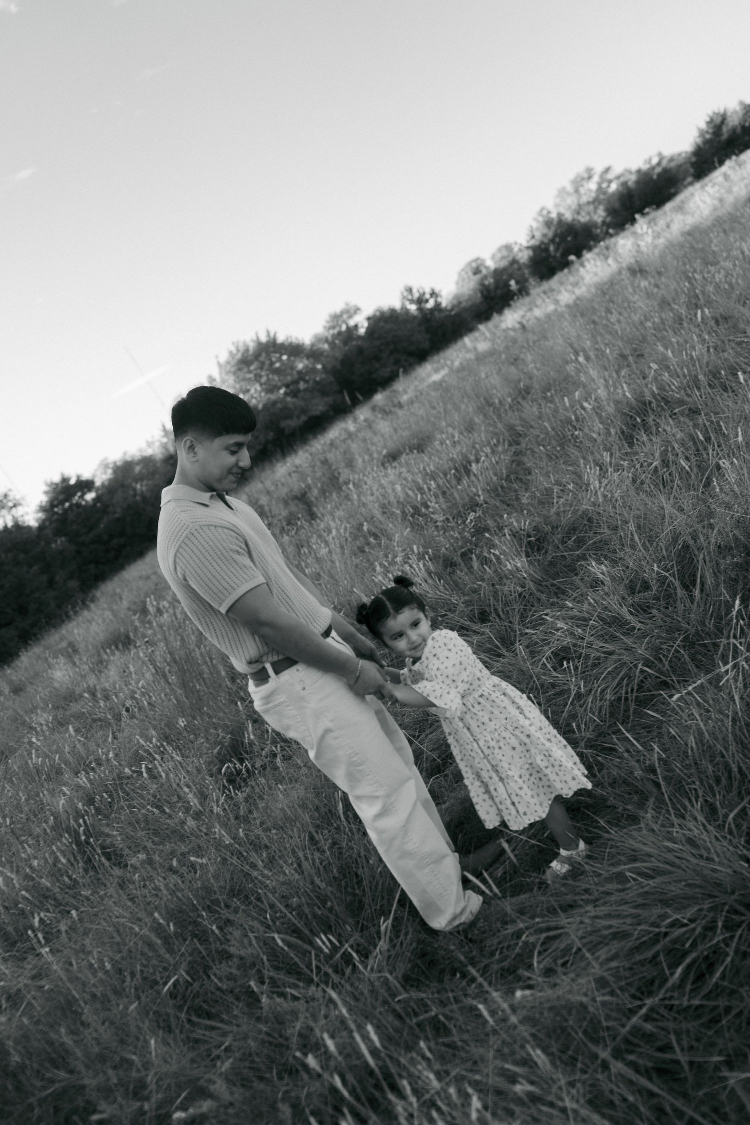 A black and white photo of a father and young daughter playing together in a grassy field at dusk.