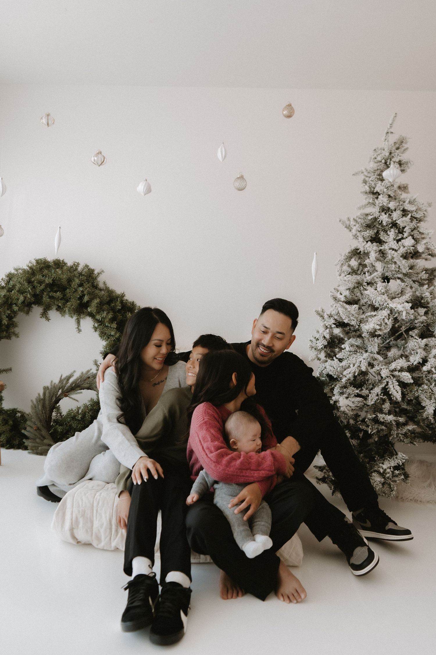An Asian family of five shares a warm embrace during a cozy Christmas photo session indoors.