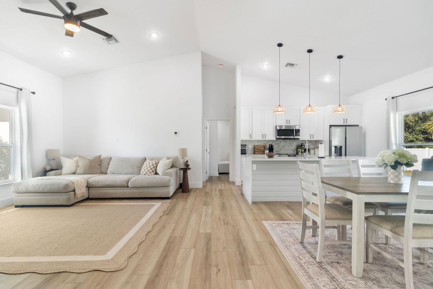 Modern open concept living space with light hardwood floors, white walls, sectional sofa and pendant lighting over kitchen island.
