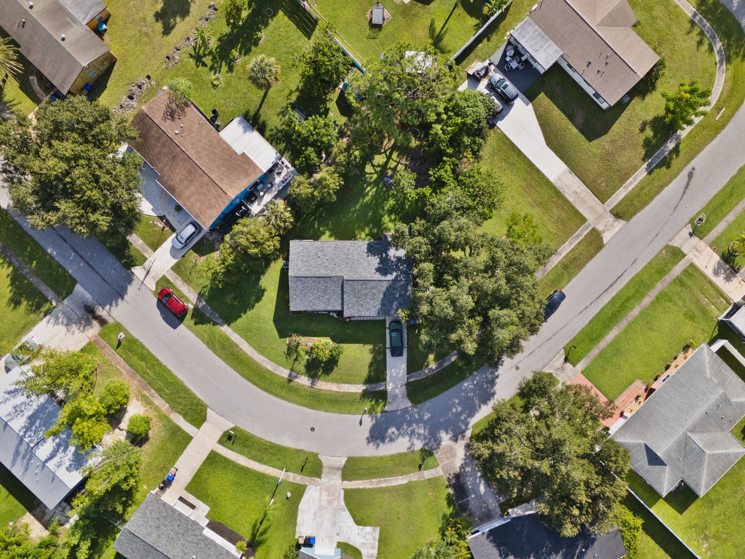 Aerial view of suburban neighborhood with green lawns and residential homes arranged along curved streets.