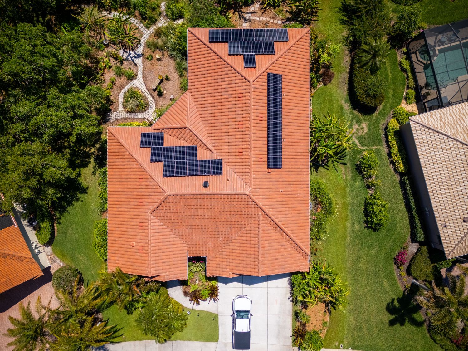 Aerial view of a Florida home with terracotta roof tiles and solar panels installed, surrounded by lush green landscaping.