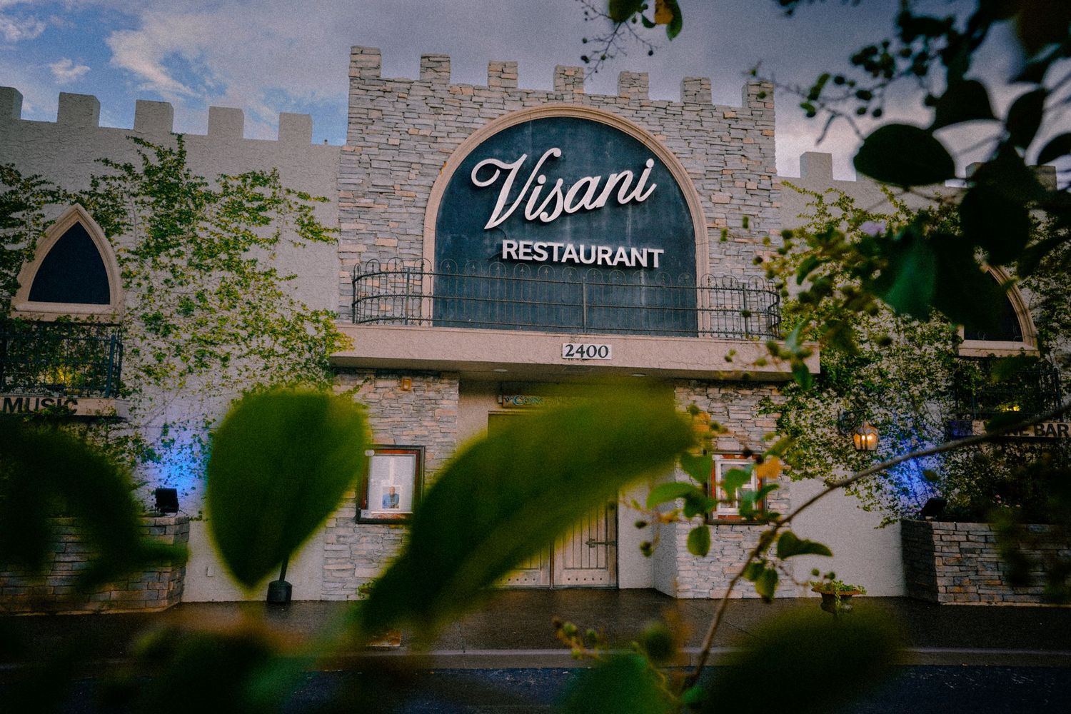 Elegant restaurant facade with decorative signage viewed through tree branches.