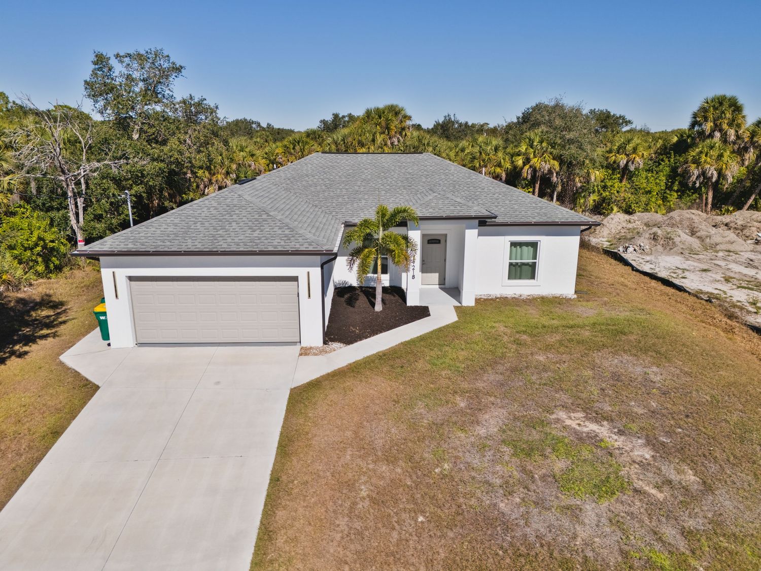 Aerial view of a modern white stucco ranch-style home with a two-car garage, palm trees, and a concrete driveway in Florida.