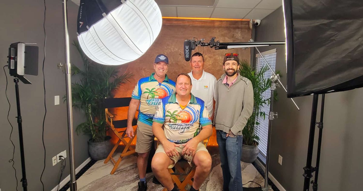 Three men pose for a professional photo shoot in a photography studio with bright lighting equipment and wooden bench.