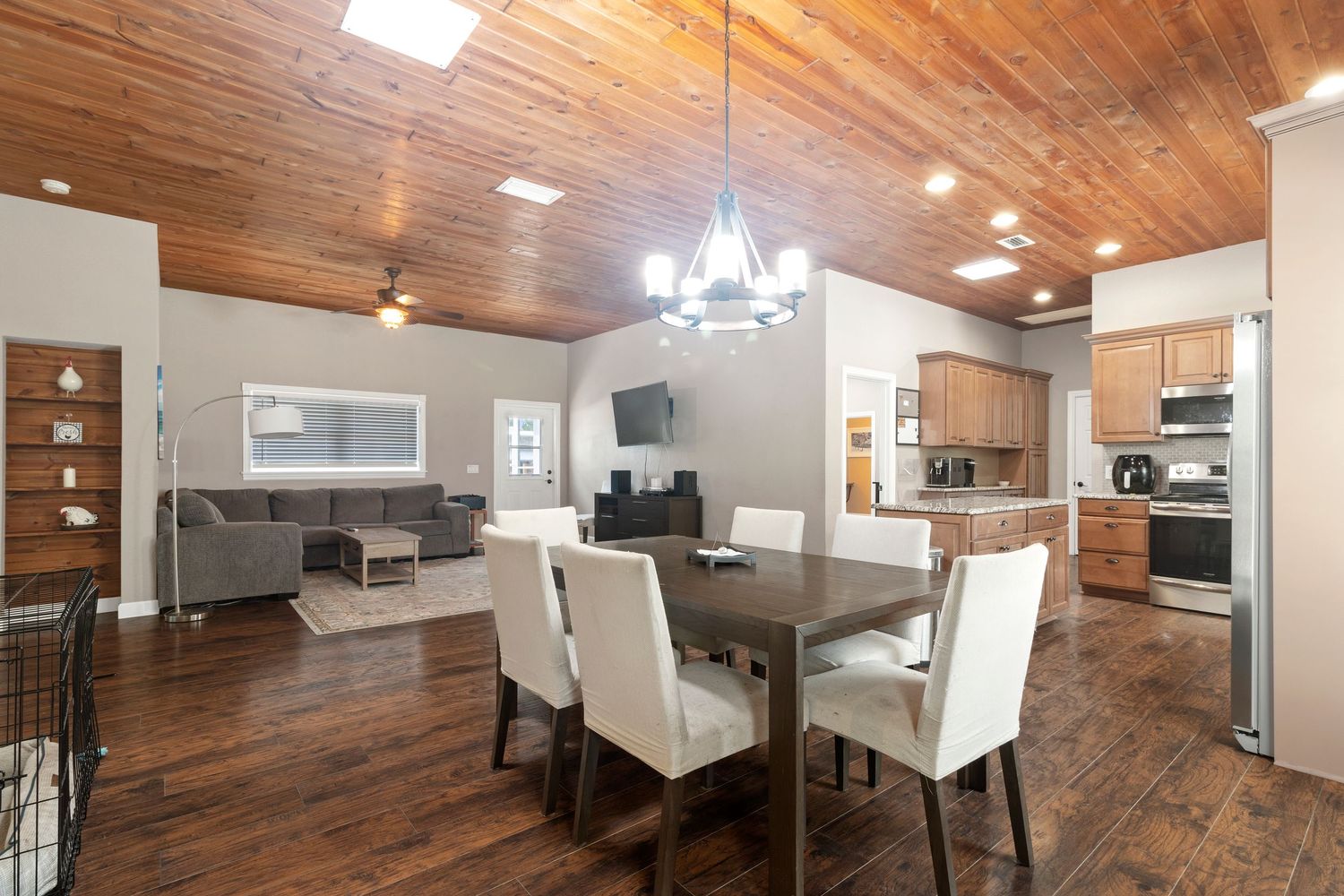 A cozy and modern open-concept living space with a wooden ceiling, recessed lighting, and a dining area with white chairs.