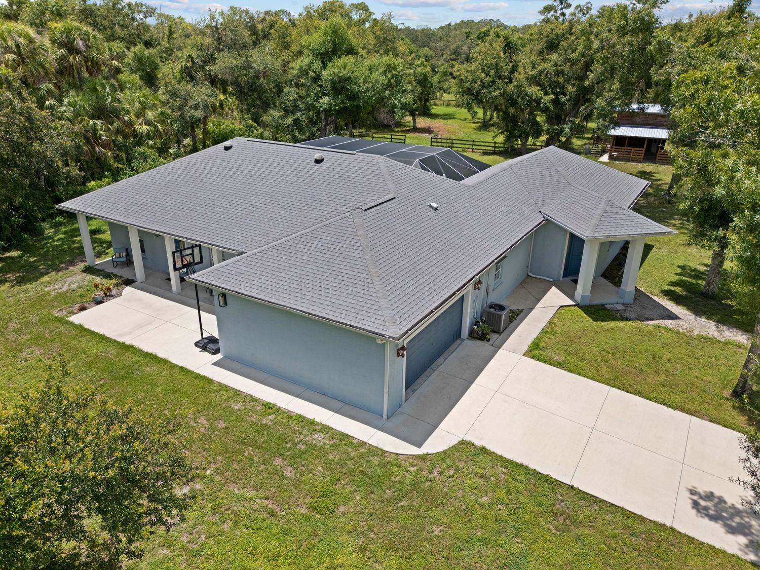 This image shows a large, modern single-story house with a gray roof, surrounded by lush greenery and trees.