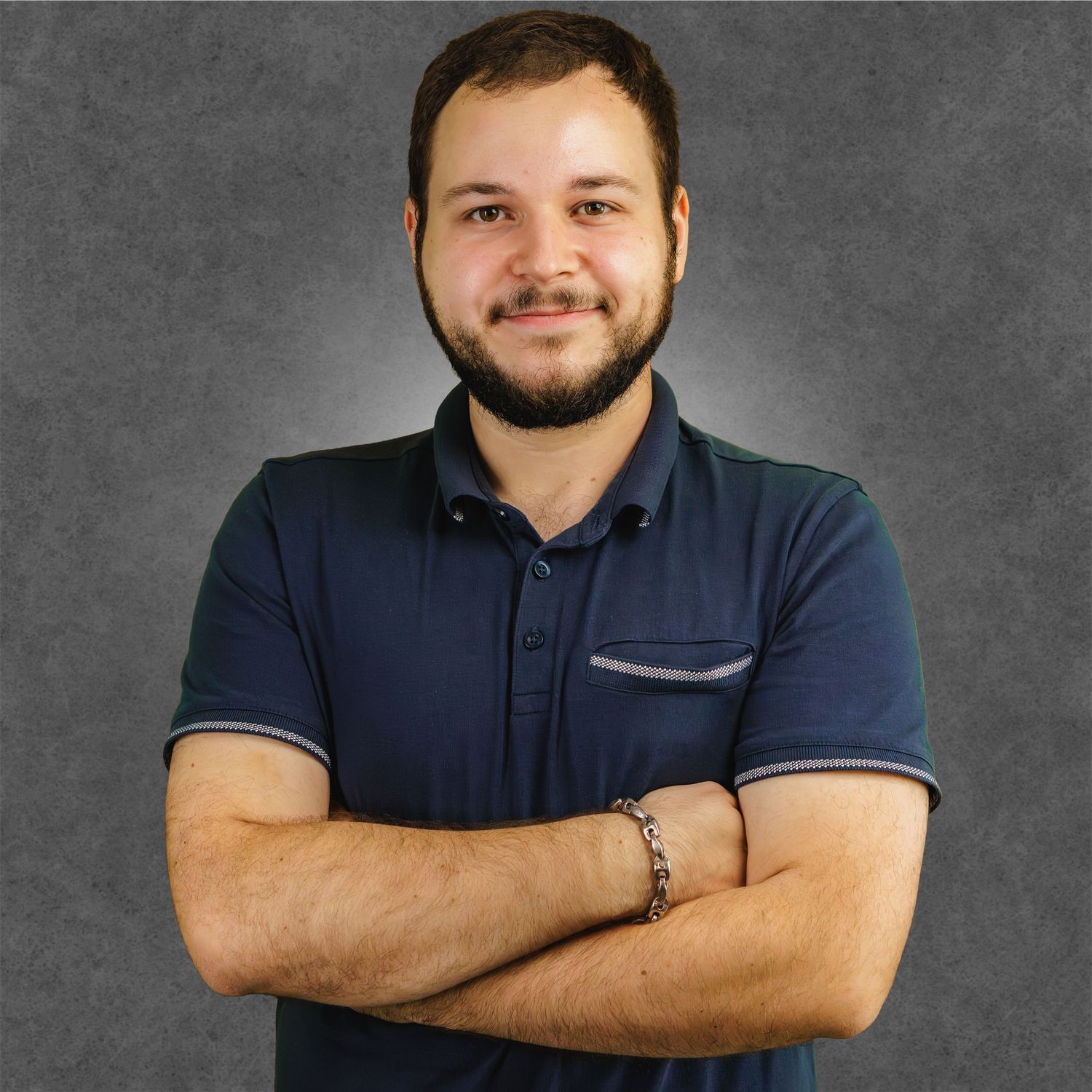 Professional headshot of someone in a navy polo shirt against a gray background smiling warmly at the camera.