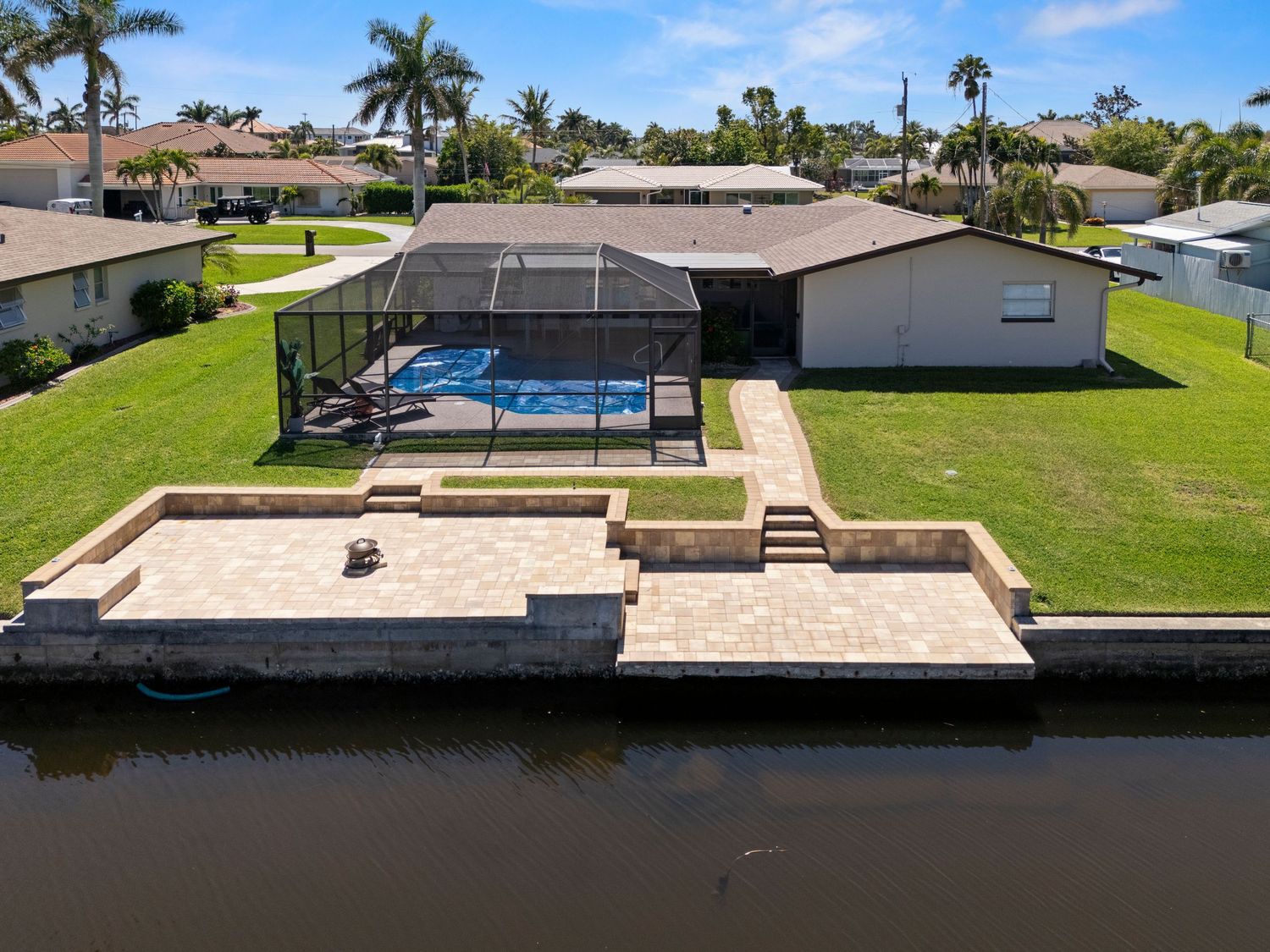 Aerial view of a waterfront home with screened pool, paver patio, and private dock on a Florida canal.