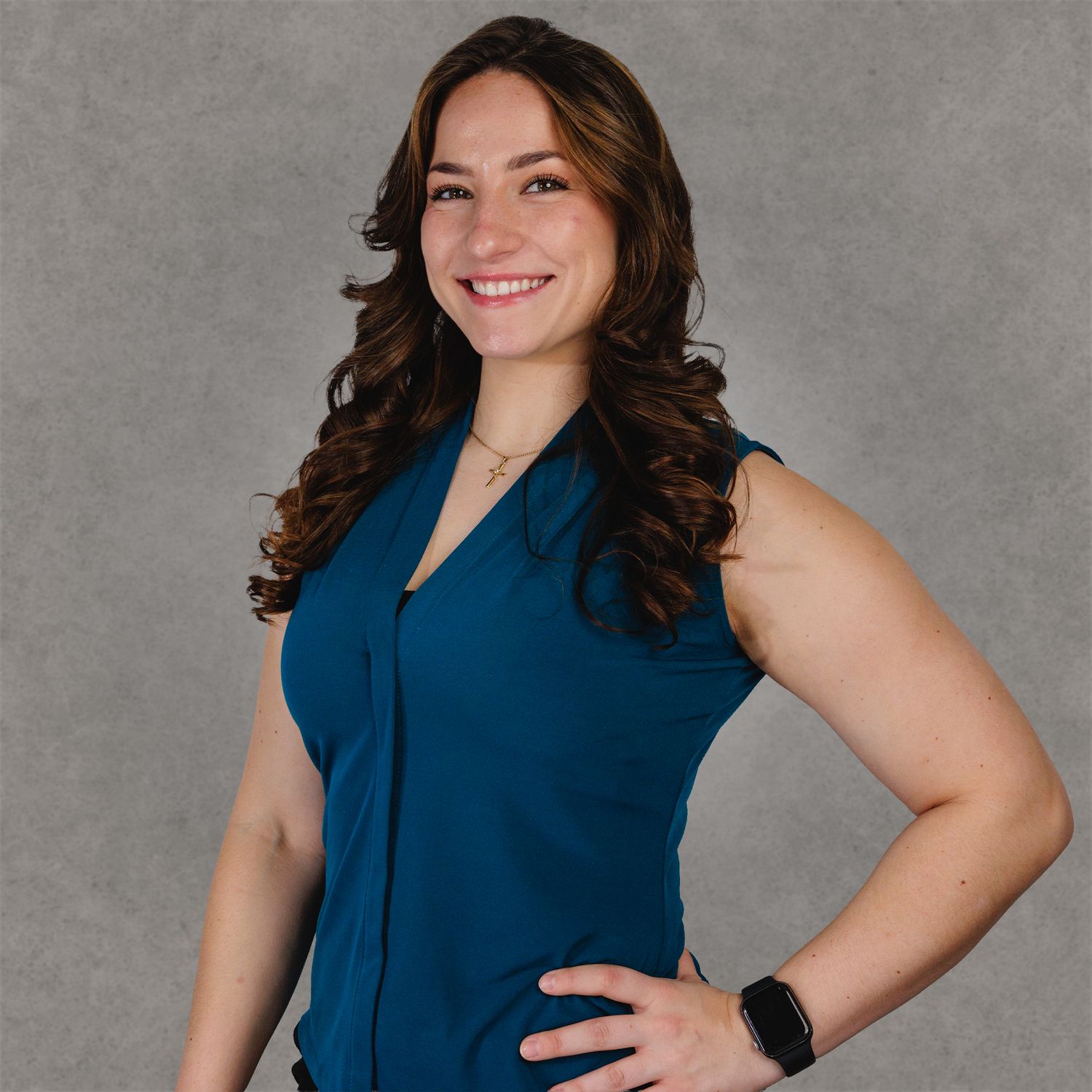 Professional woman in teal sleeveless blouse smiling confidently against gray background.