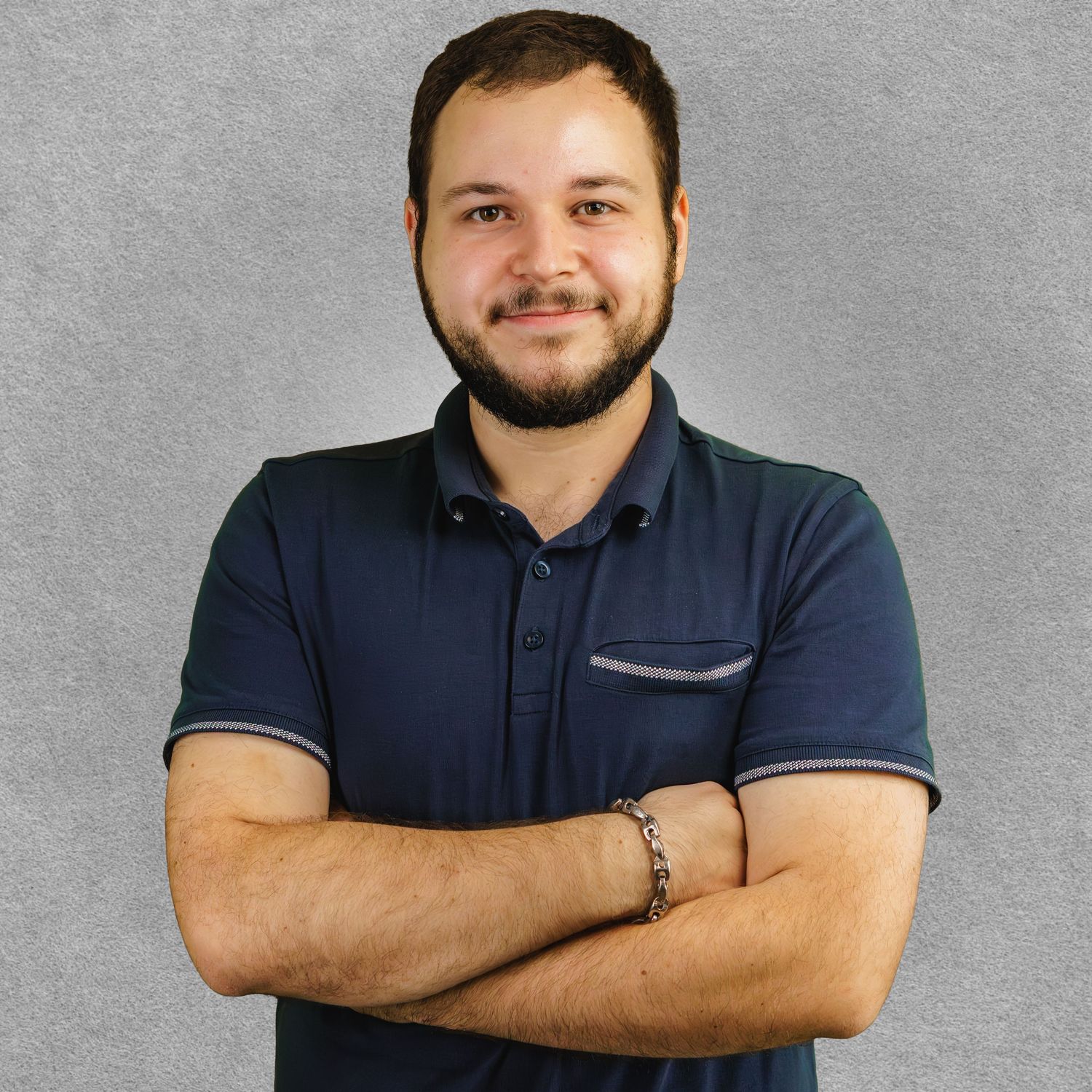 Professional headshot of person in navy polo shirt with crossed arms against gray background.