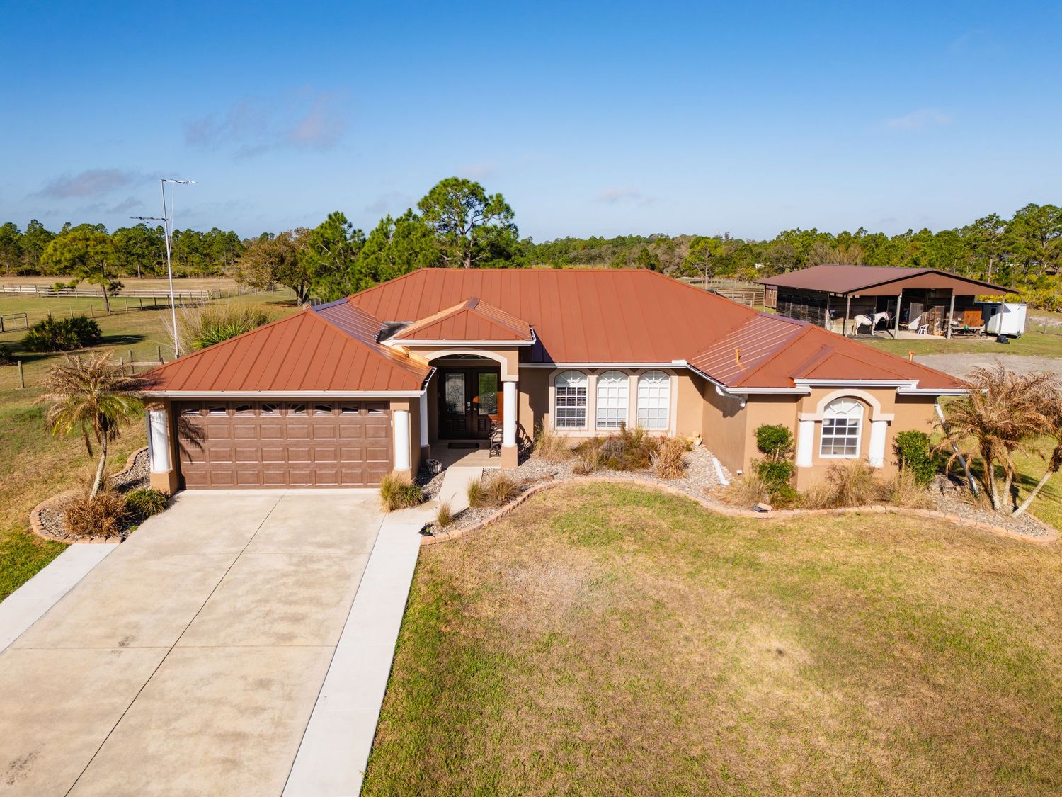 Aerial view of a single-story ranch house with red tile roof and attached garage in a rural setting.