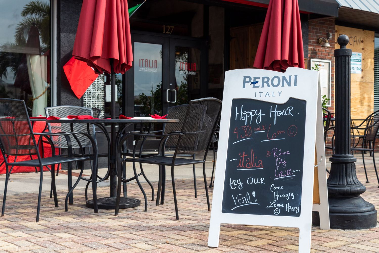 Red patio umbrellas and outdoor seating area at a restaurant with chalkboard menus.
