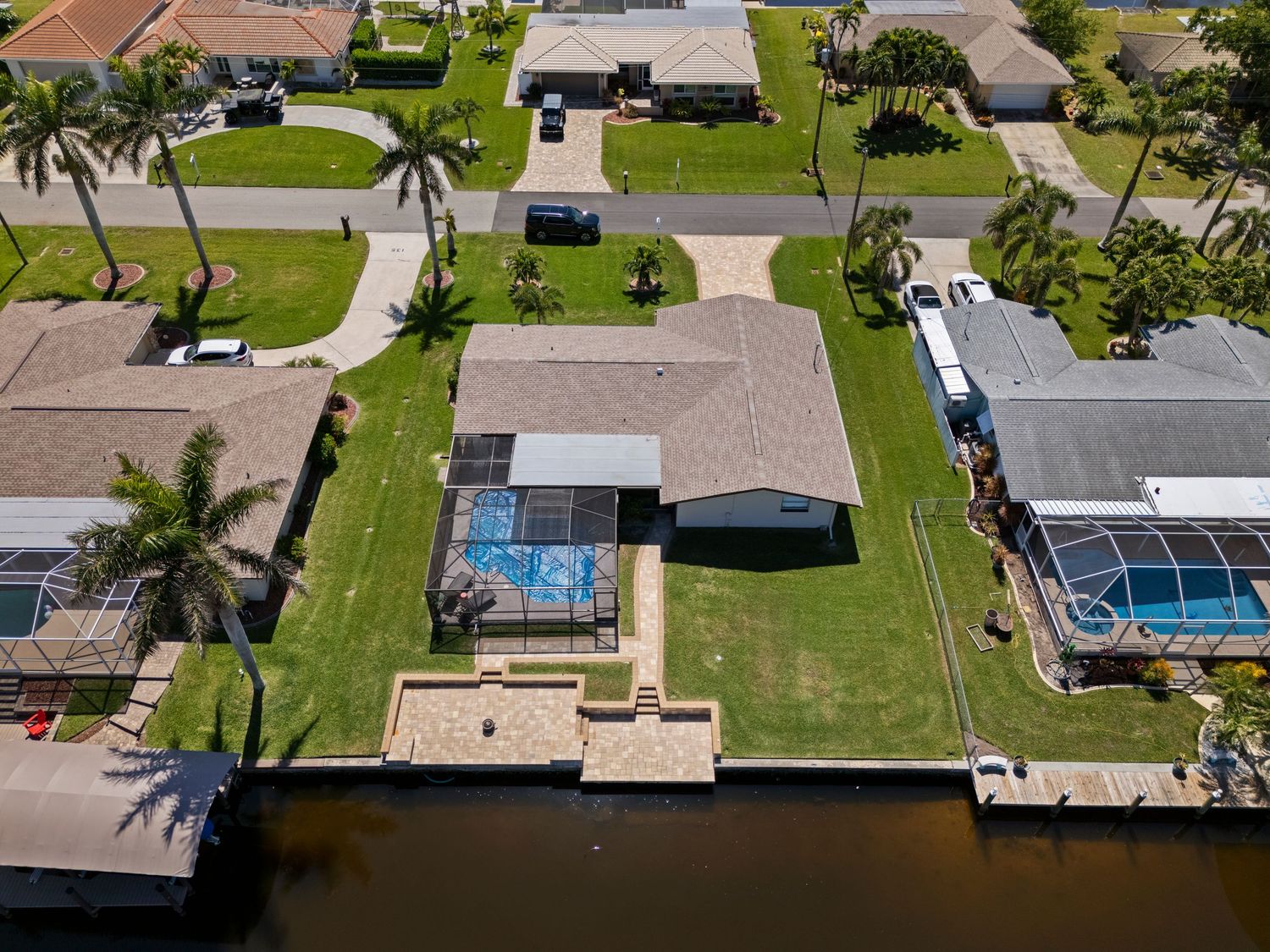 Aerial view of waterfront homes with pools, docks, and palm trees along a canal in a suburban neighborhood.