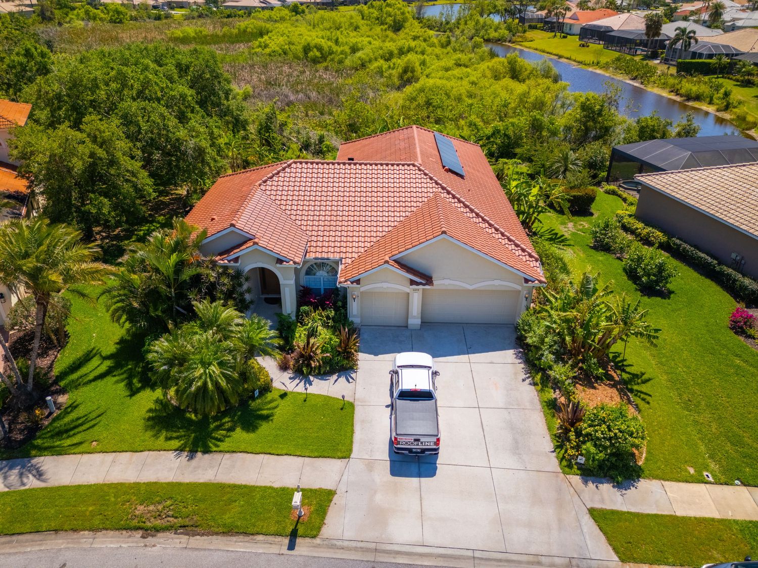 Aerial view of a large residential home with a red tile roof surrounded by lush green landscaping and a paved driveway.