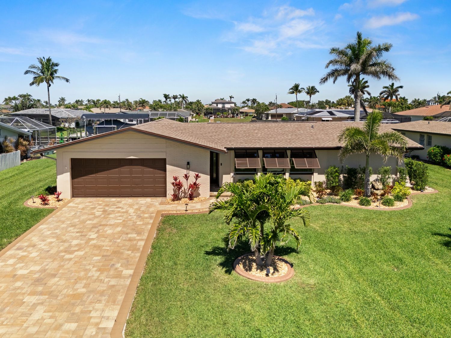 Aerial view of a brown single-story Florida home with palm trees, lush lawn and paver driveway in a residential neighborhood.