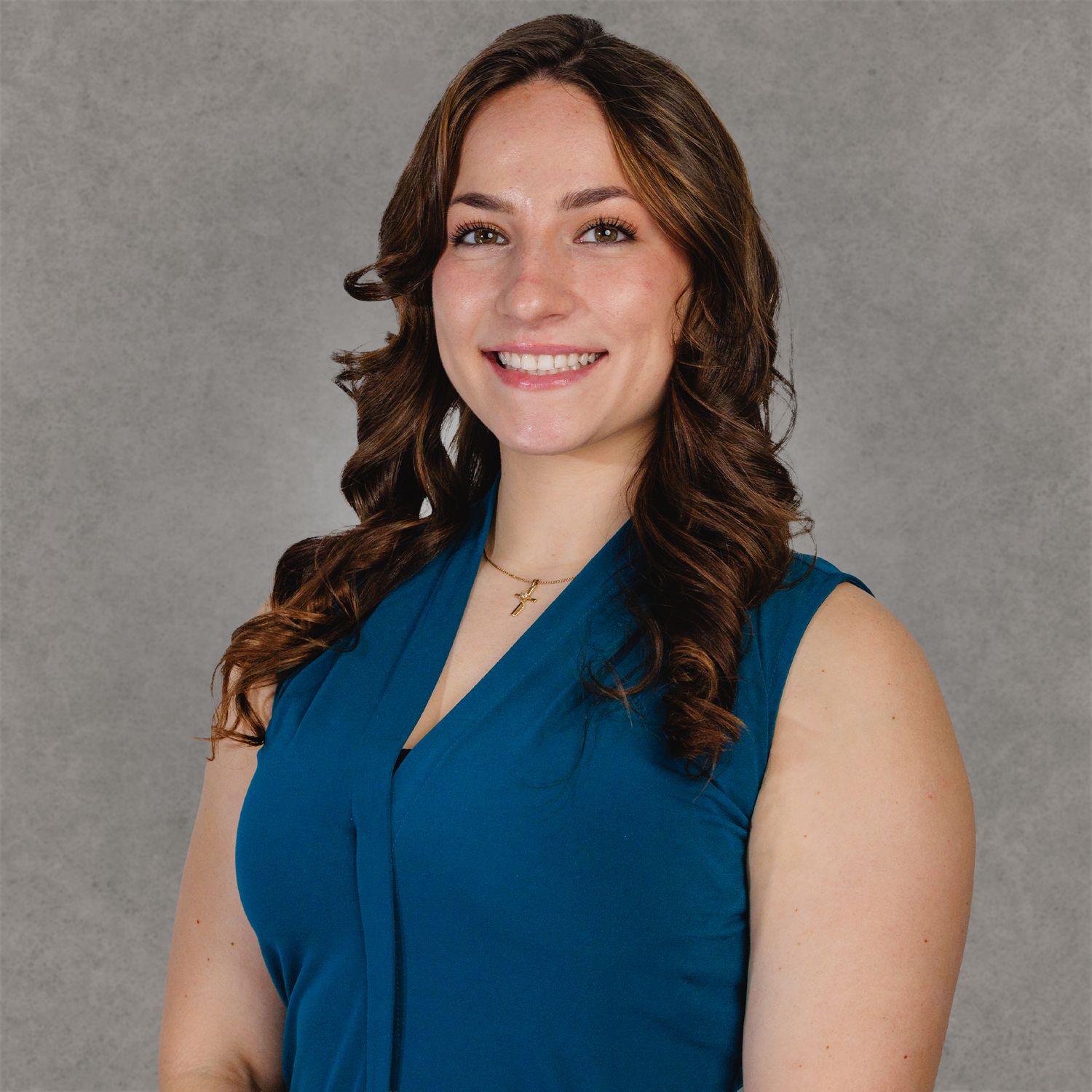 Professional headshot of a smiling woman with curly brown hair wearing a teal sleeveless blouse and delicate necklace.